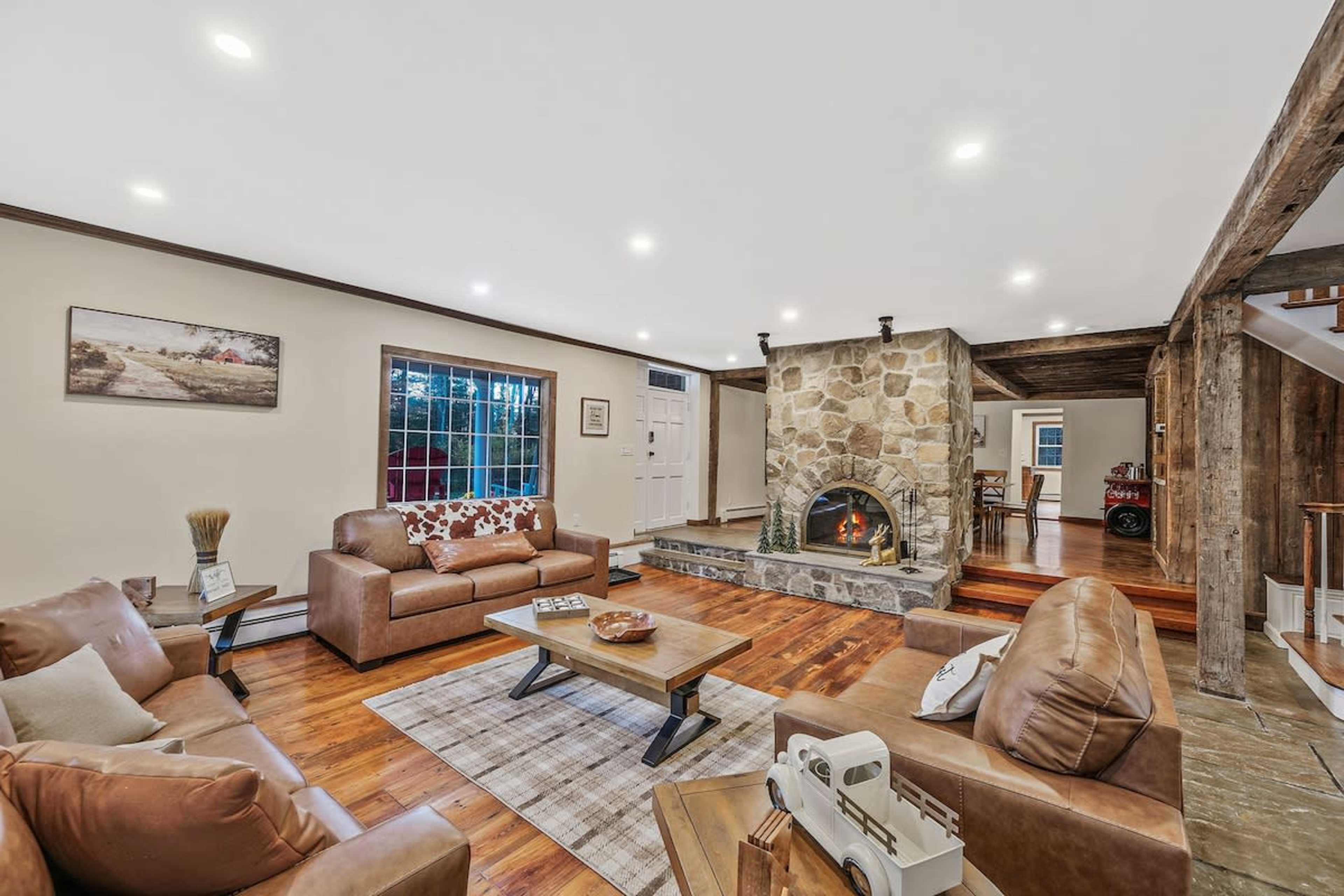 The image shows a spacious living room featuring a stone fireplace, wooden flooring, and leather furniture arranged around a central coffee table.
