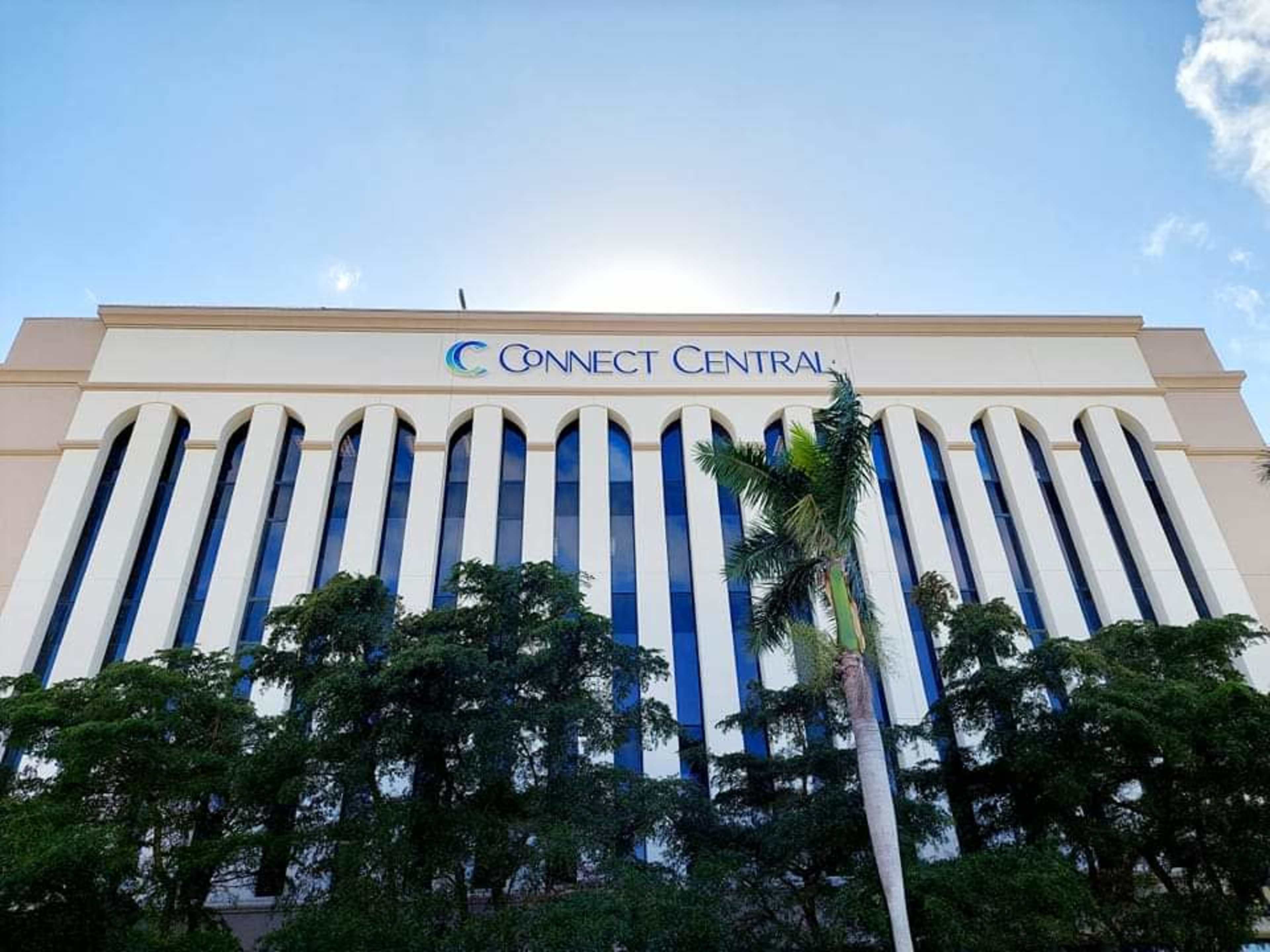 A large building with a sign reading "Connect Central" features multiple vertical windows adorned with palm trees in the foreground.