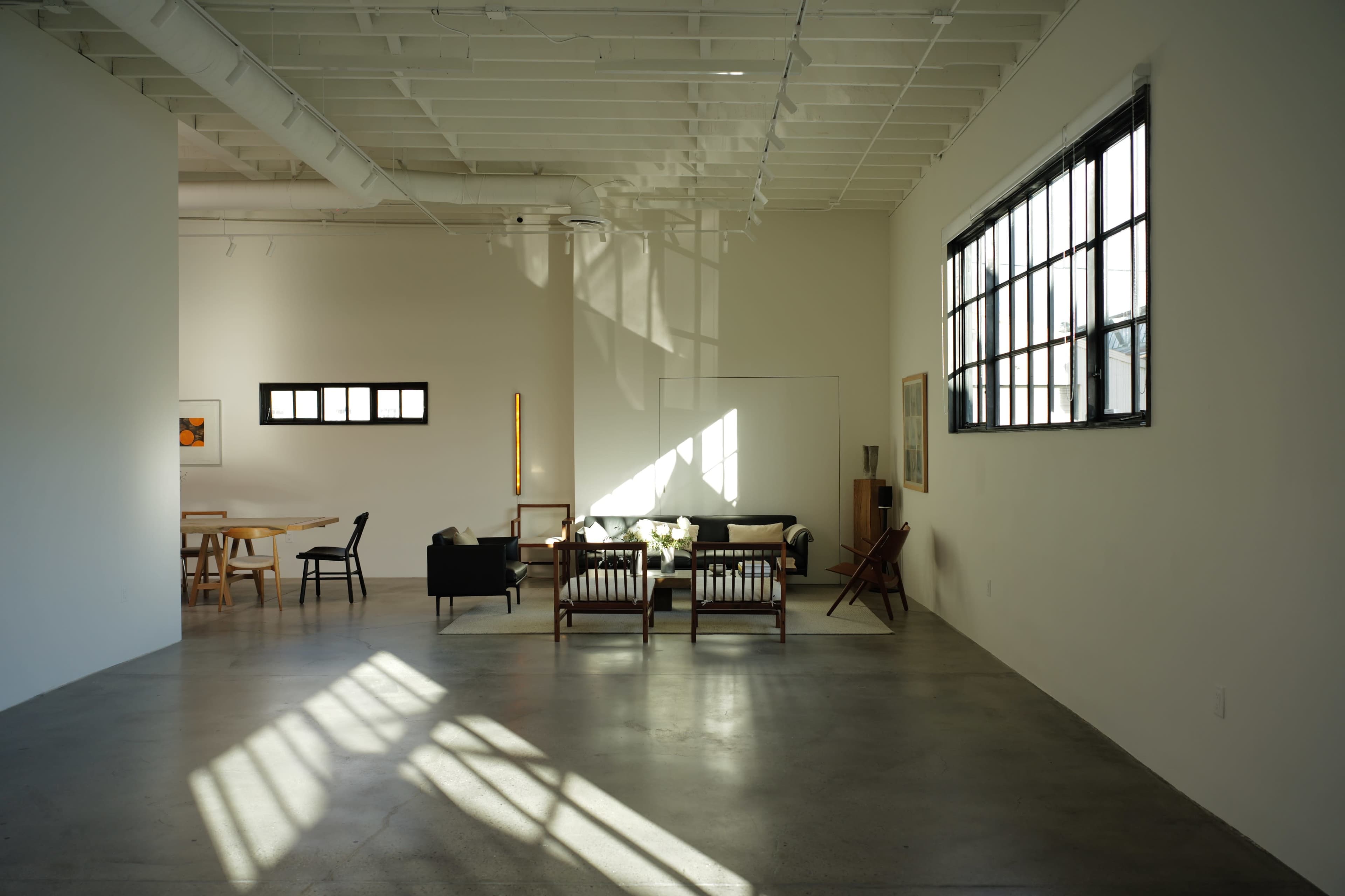 The image shows a spacious, modern living area with minimalist furniture, large windows, and polished concrete floors.