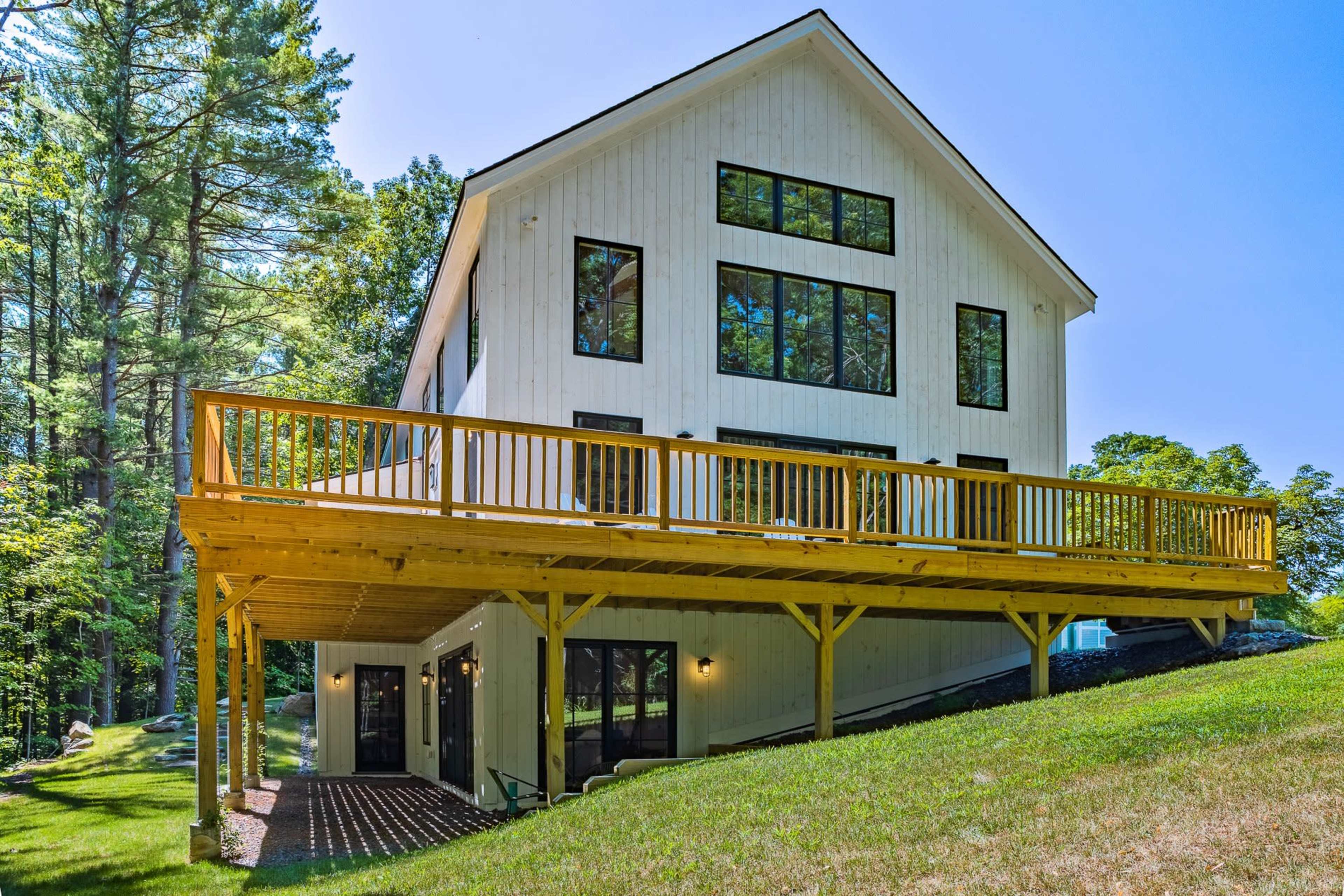A modern two-story house with large windows and a wooden deck in a wooded setting.