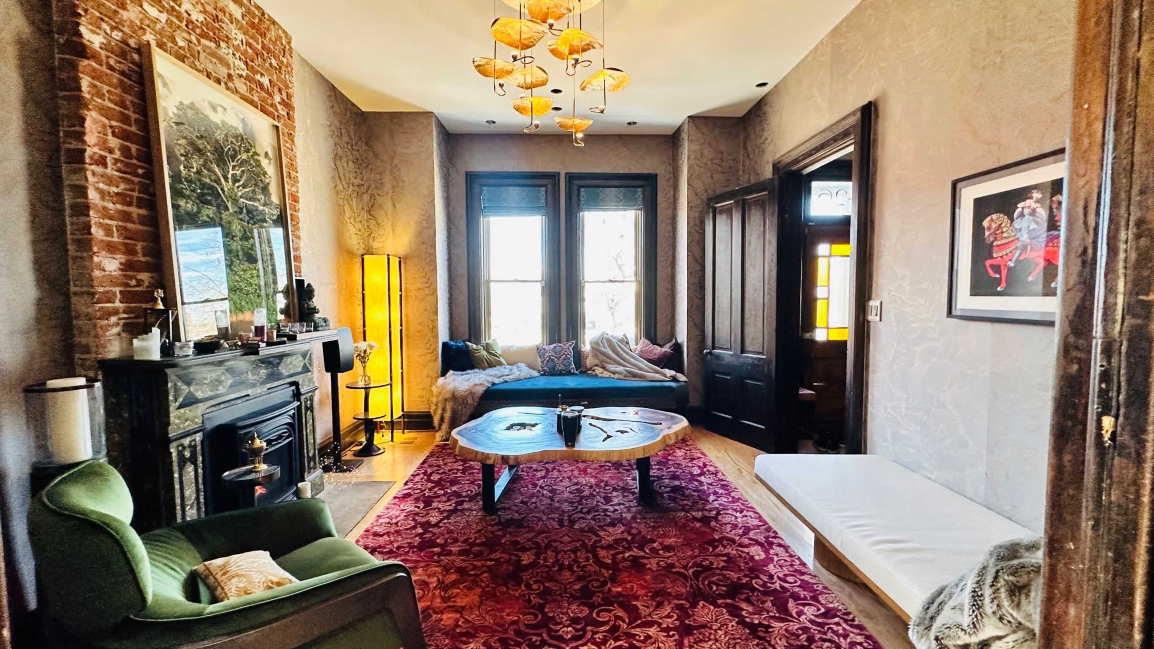 A living room with a brick accent wall, a fireplace, a large decorative rug, and a mix of modern and vintage furniture.