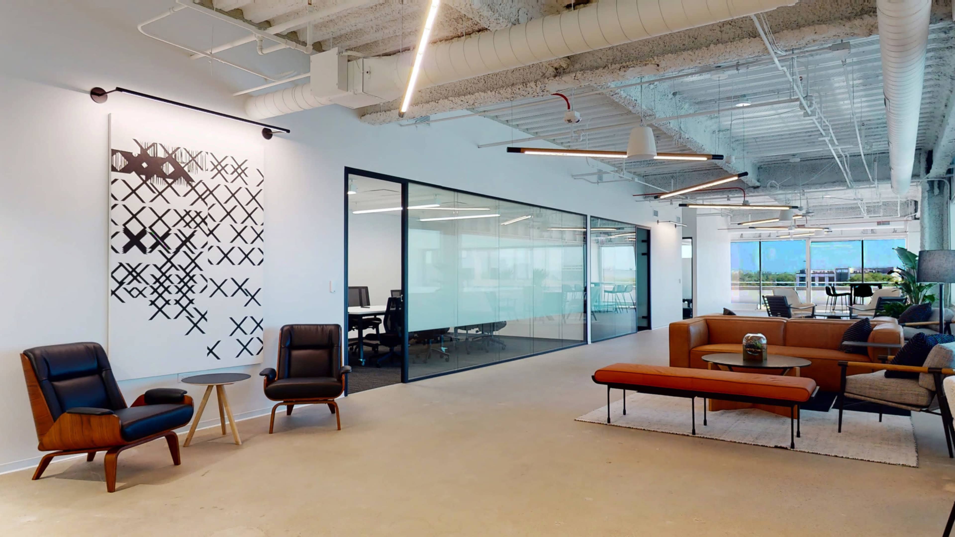 A modern office space featuring a seating area with various styles of furniture, a glass-walled meeting room, and abstract wall art.