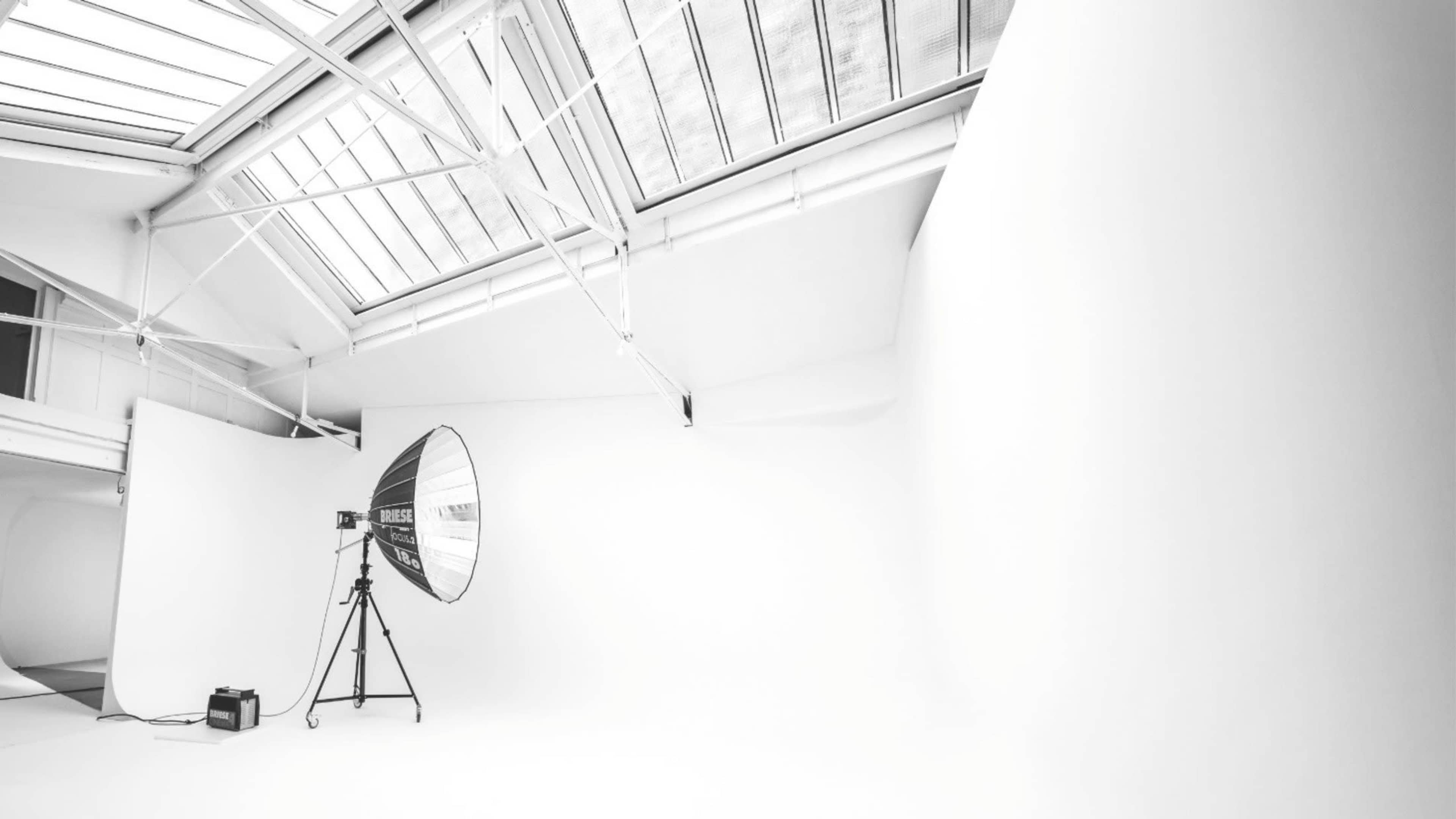The image shows a spacious photography studio with white walls and a large softbox light set up on a stand.