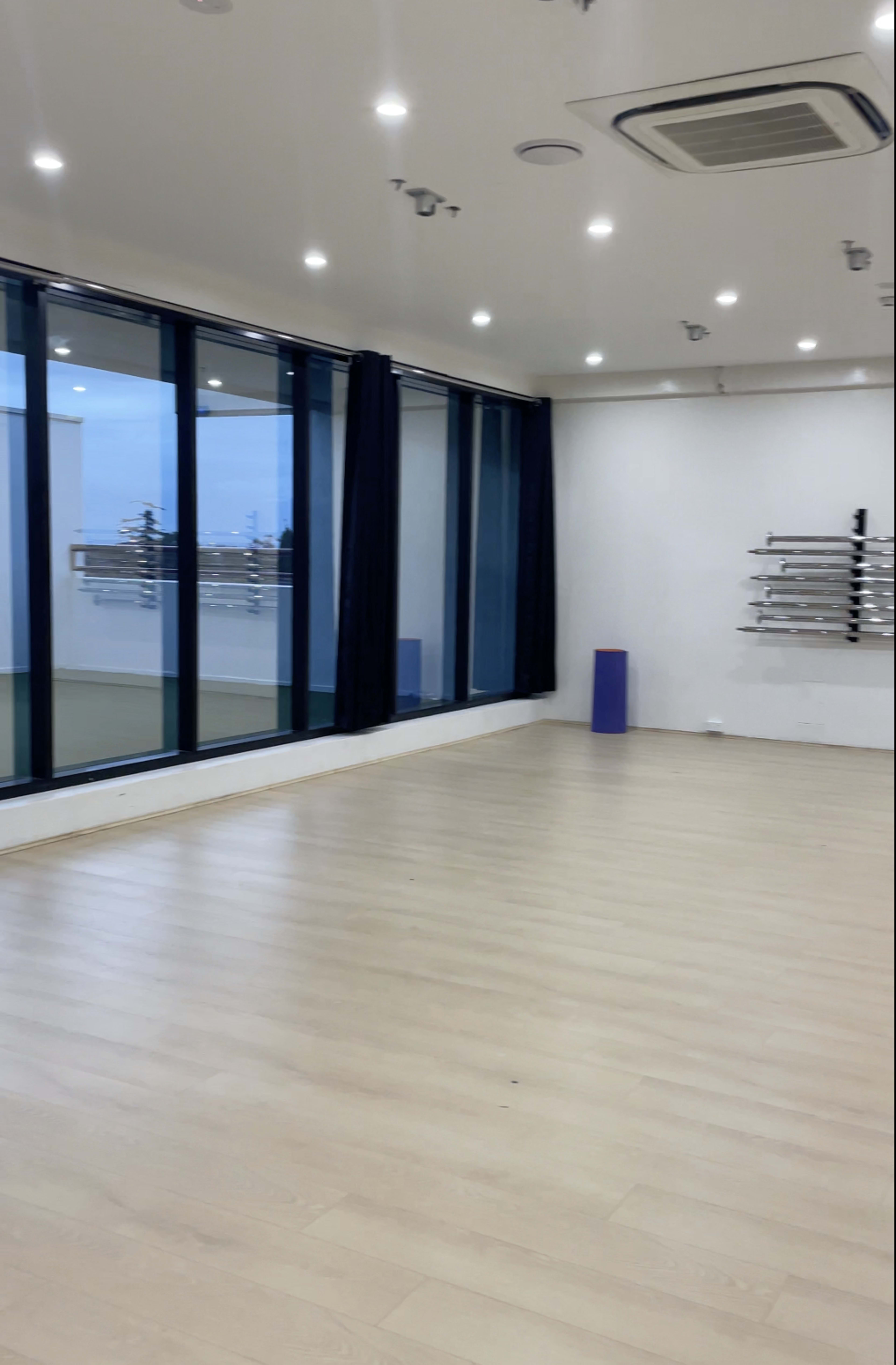 A spacious, empty room with large windows, a smooth wooden floor, and a set of shelves mounted on the wall.