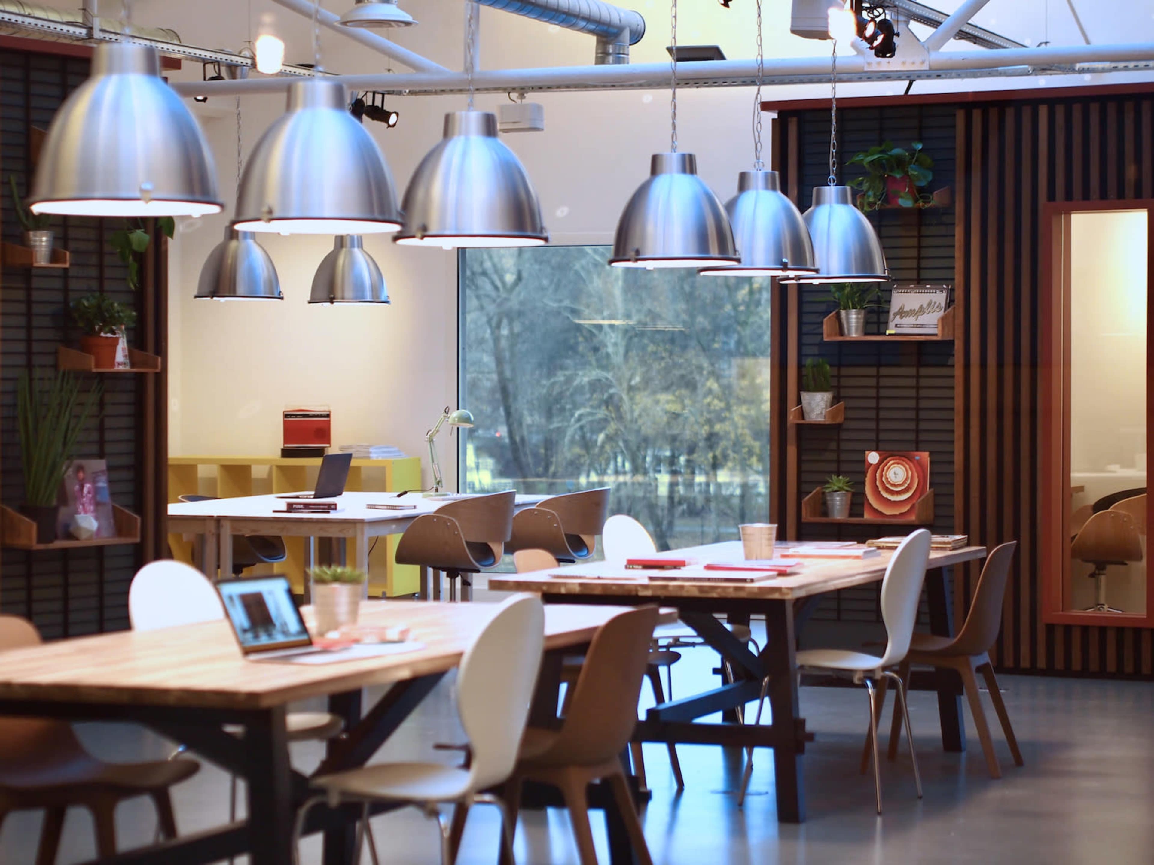 A modern office space with wooden tables, stylish chairs, and large pendant lights hanging from the ceiling.