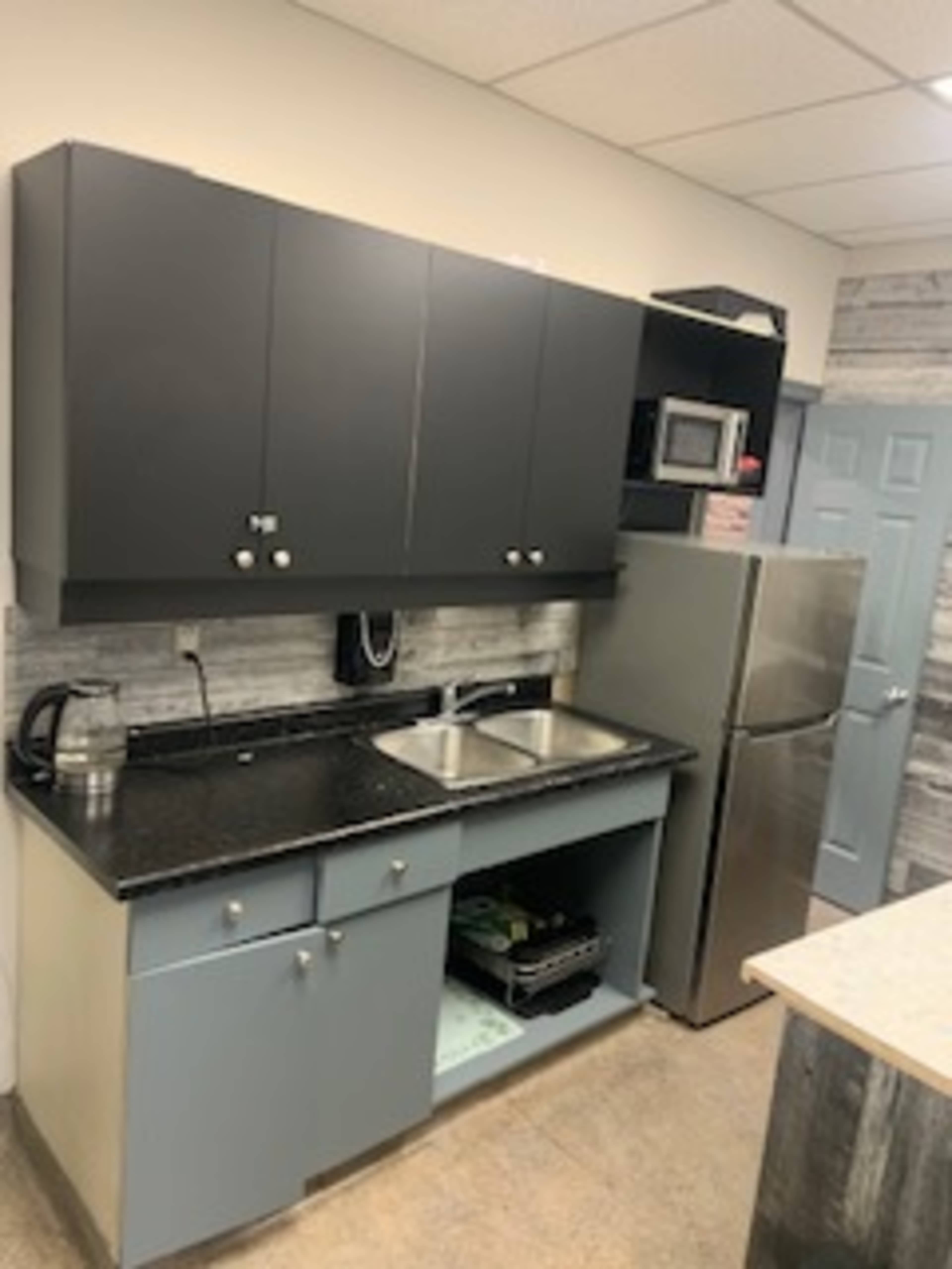 The image shows a modern kitchen with dark cabinets, a double sink, a stainless steel refrigerator, and a countertop with a textured design.