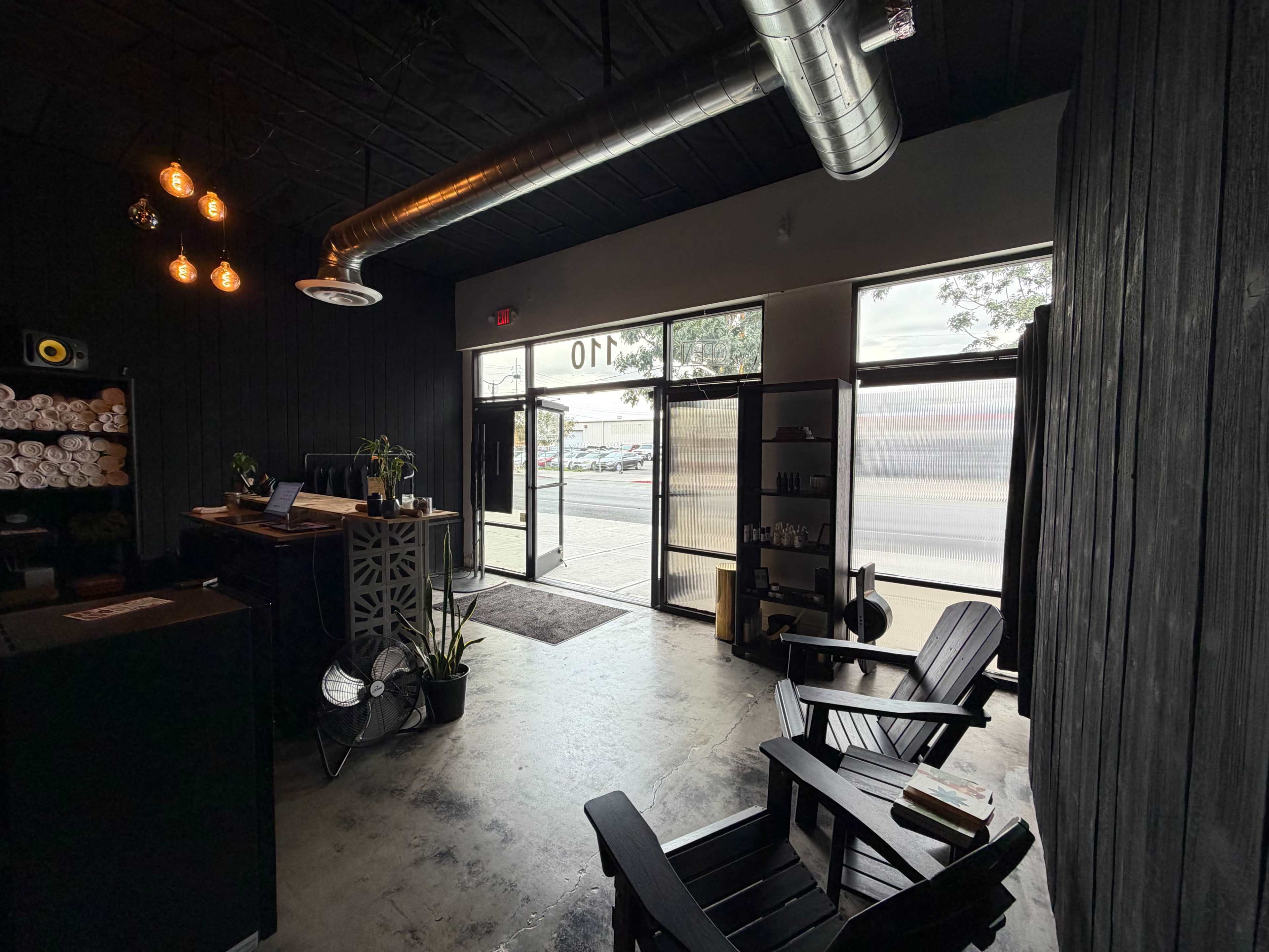 The image shows a modern, minimalist reception area with two wooden chairs facing an entrance featuring large glass doors.