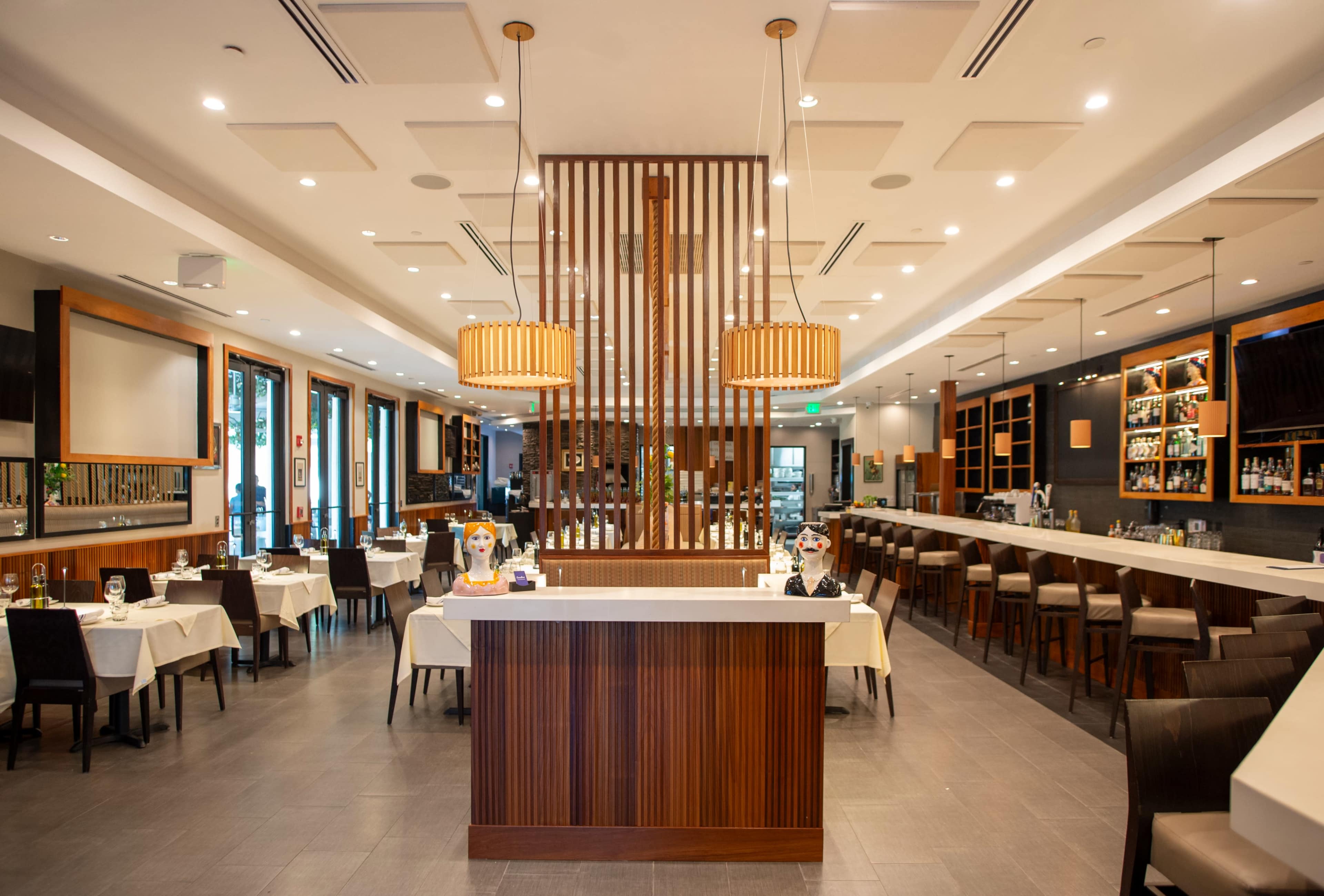 The image shows a modern restaurant interior with a central bar, wooden decor, and tables set for dining.