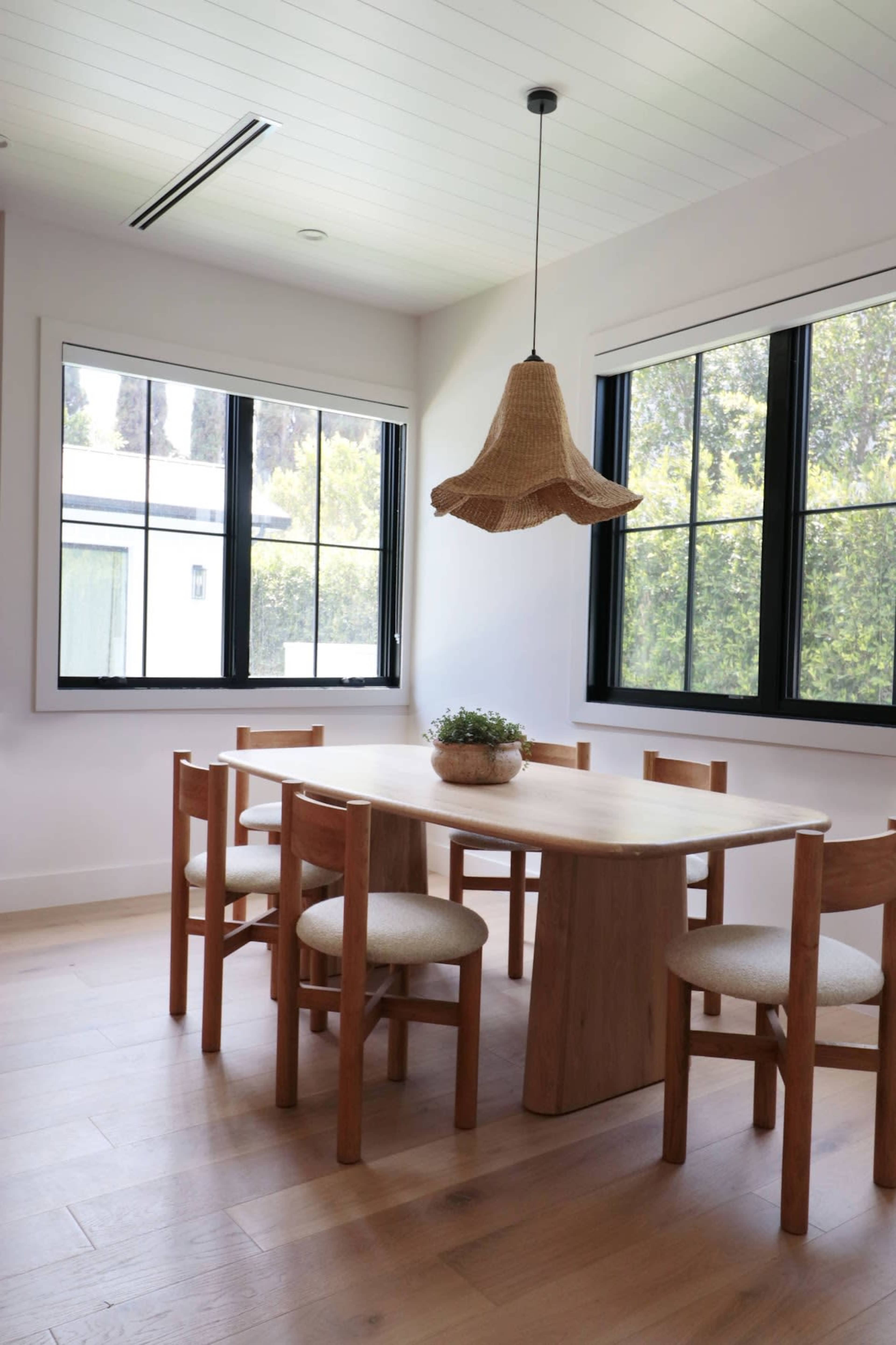 A minimalist dining area features a wooden table surrounded by six chairs and a pendant light hanging from the ceiling.