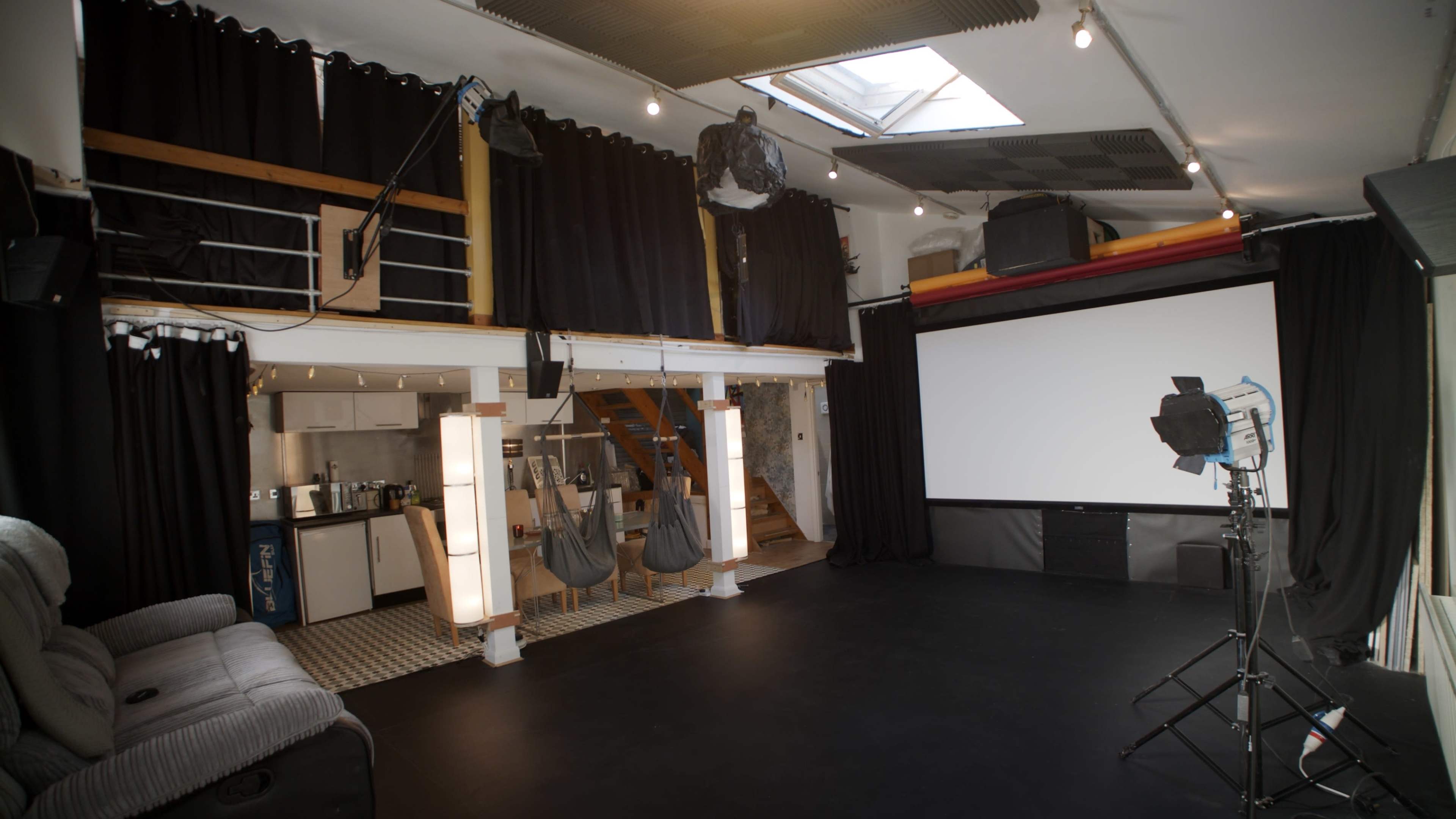 A spacious interior room with a black floor, wooden stairs leading to an upper level, and a large projection screen against one wall.
