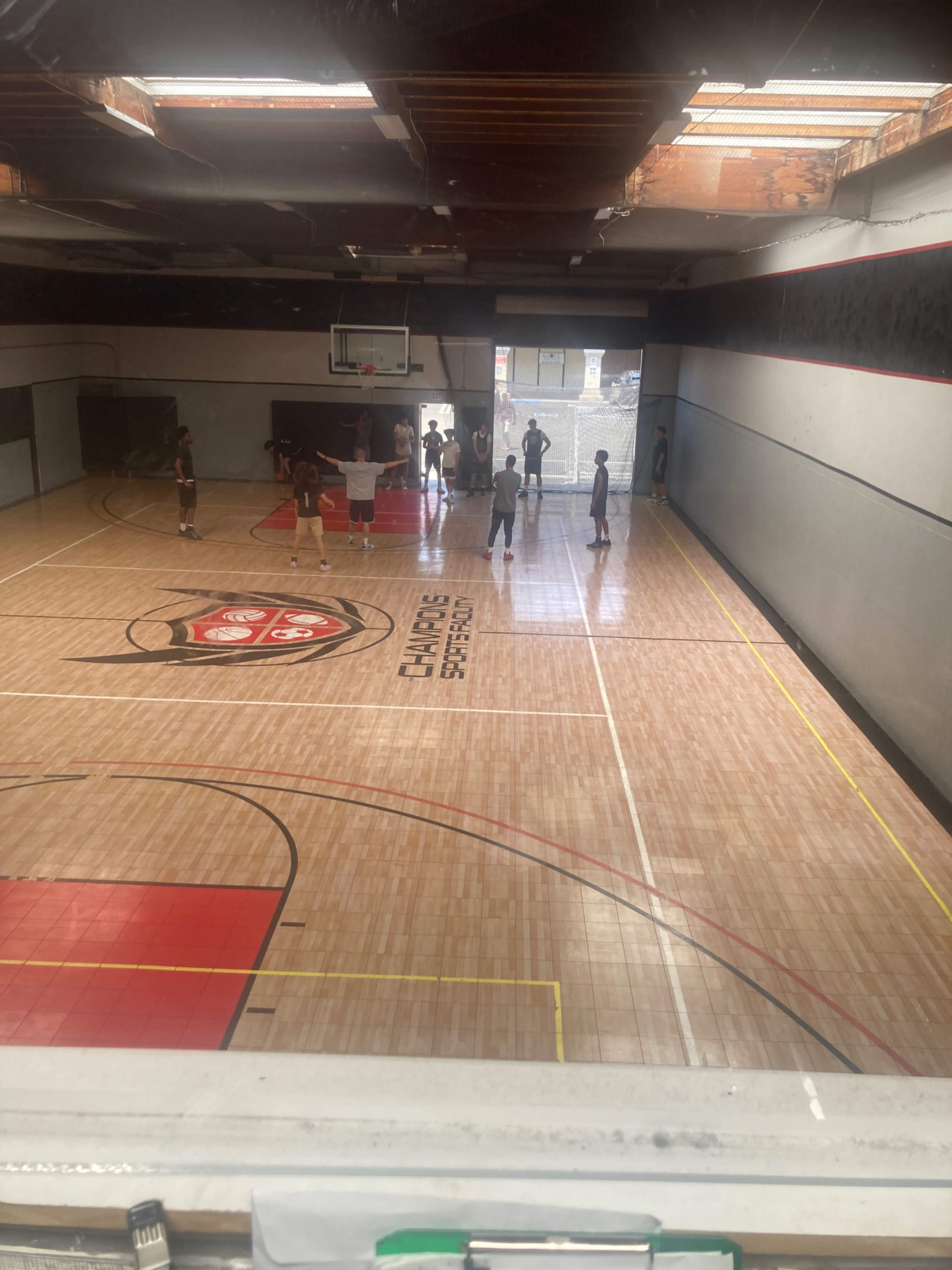 A group of people is playing basketball on a wooden court inside a gymnasium.