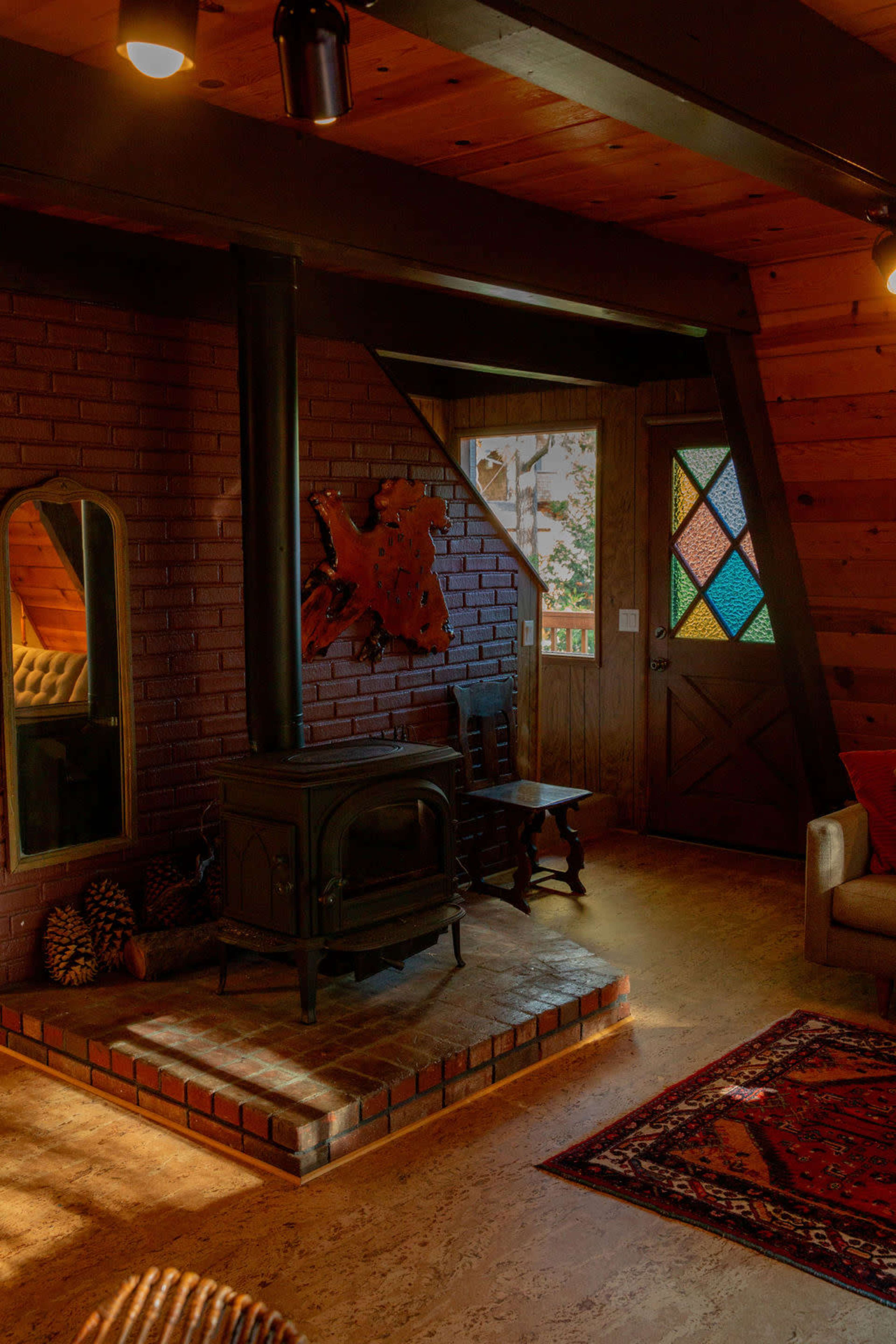 The scene shows a cozy cabin interior with a wood stove, a colorful stained-glass door, and rustic wooden beams.