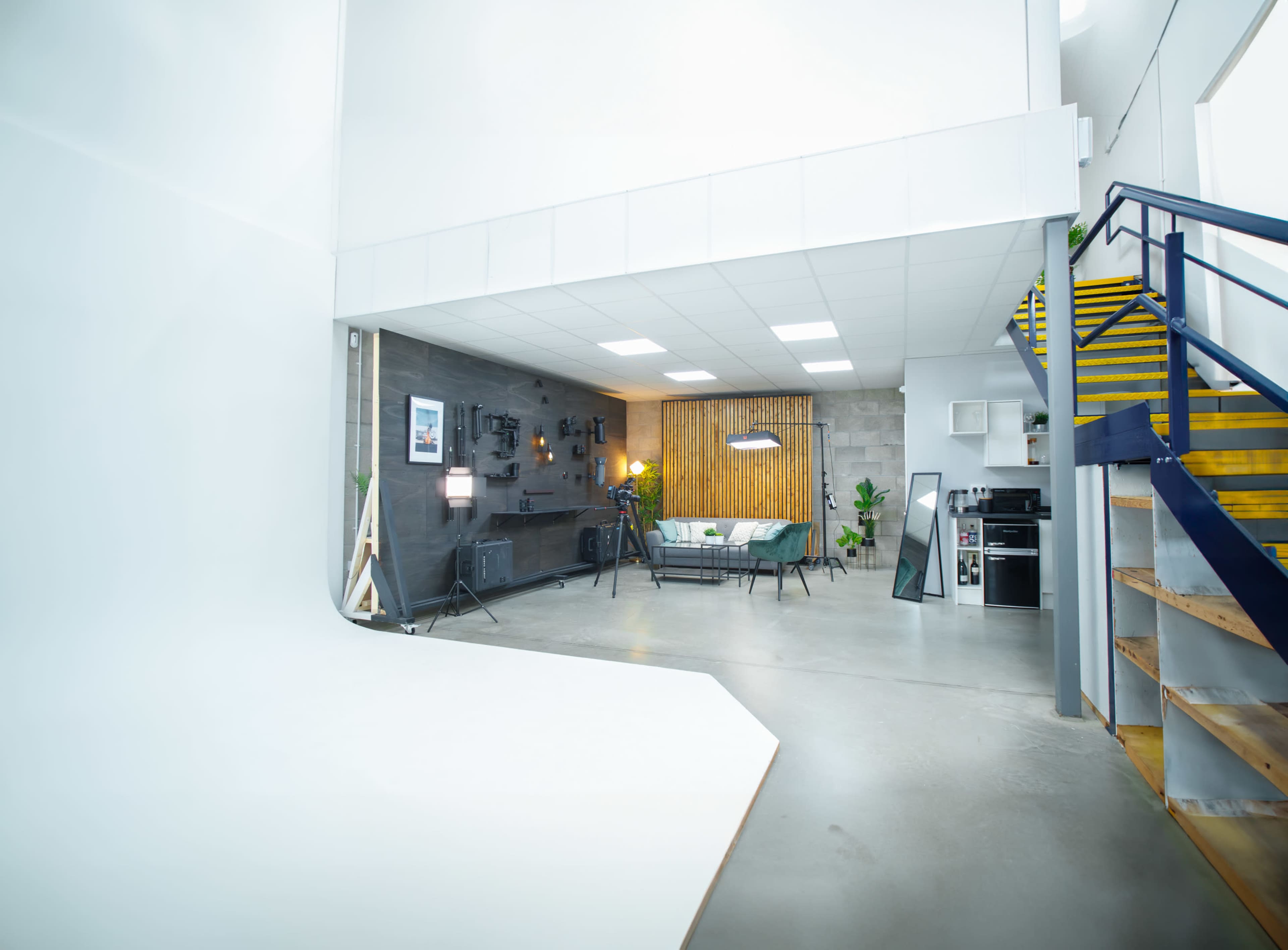 A modern, open studio space with a gray wall, wooden accents, seating area, and stairs leading to an upper level.