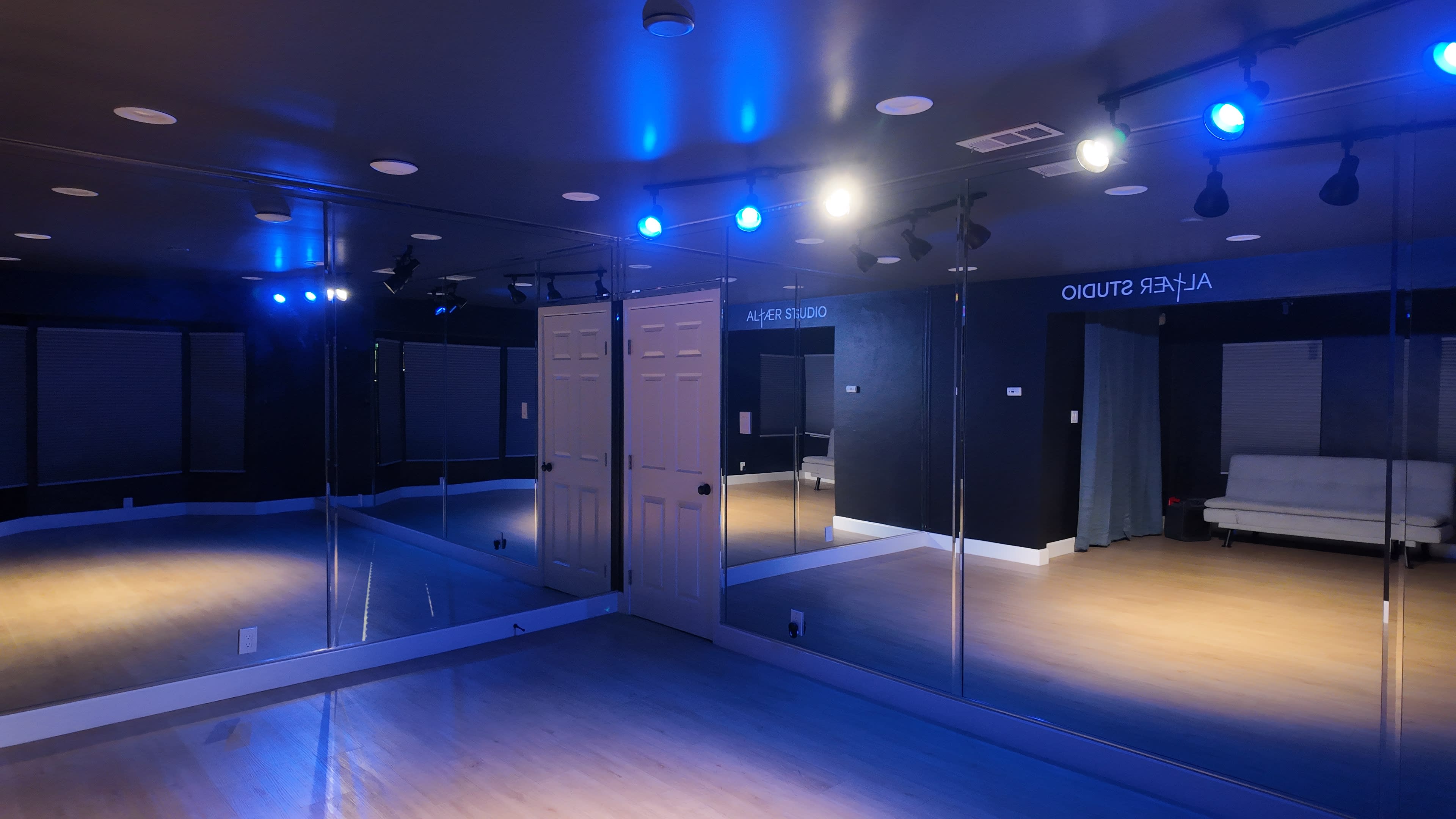 A dance studio features mirrored walls, a wooden floor, and blue overhead lights illuminating the space.