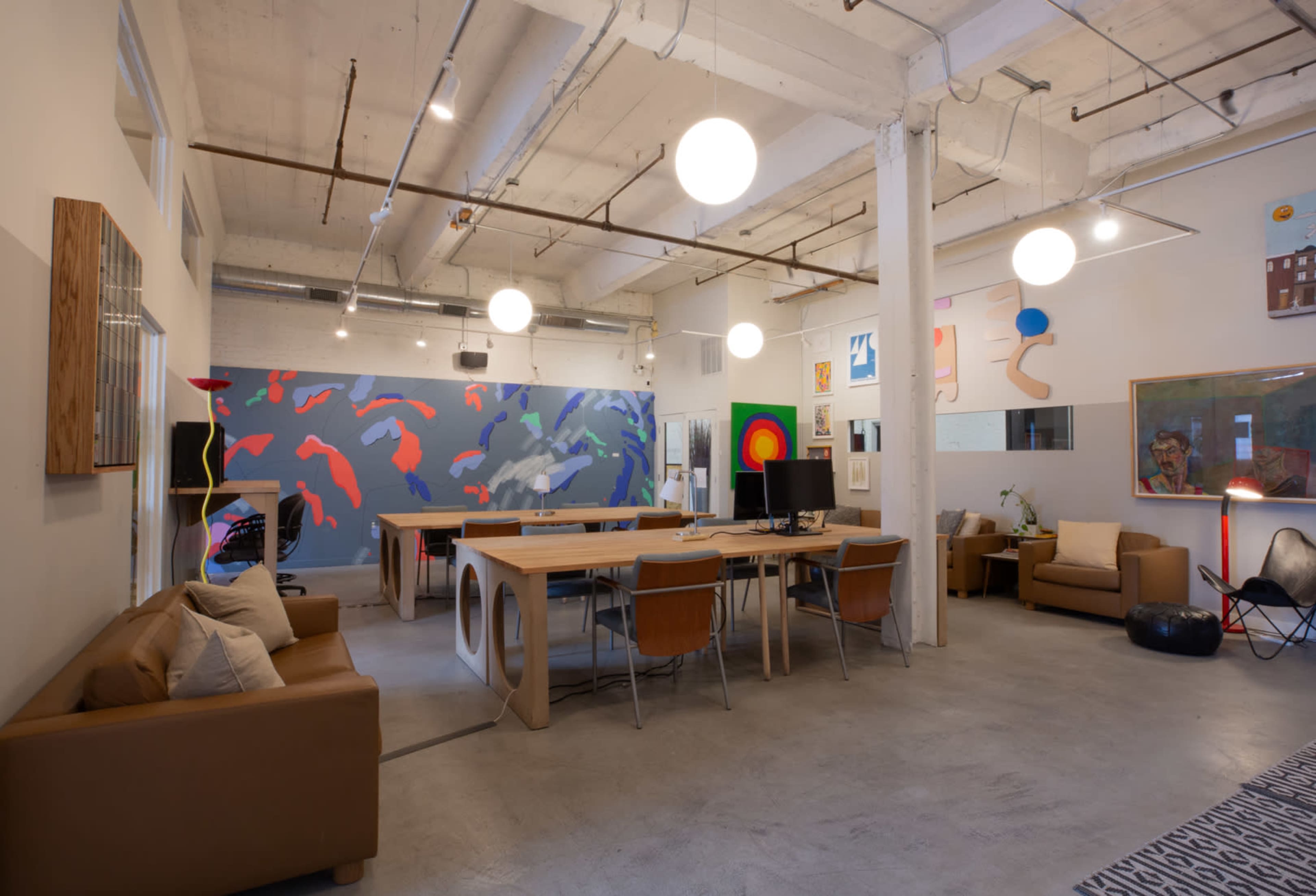 A spacious office area with a long wooden table, comfortable seating, and colorful wall art.