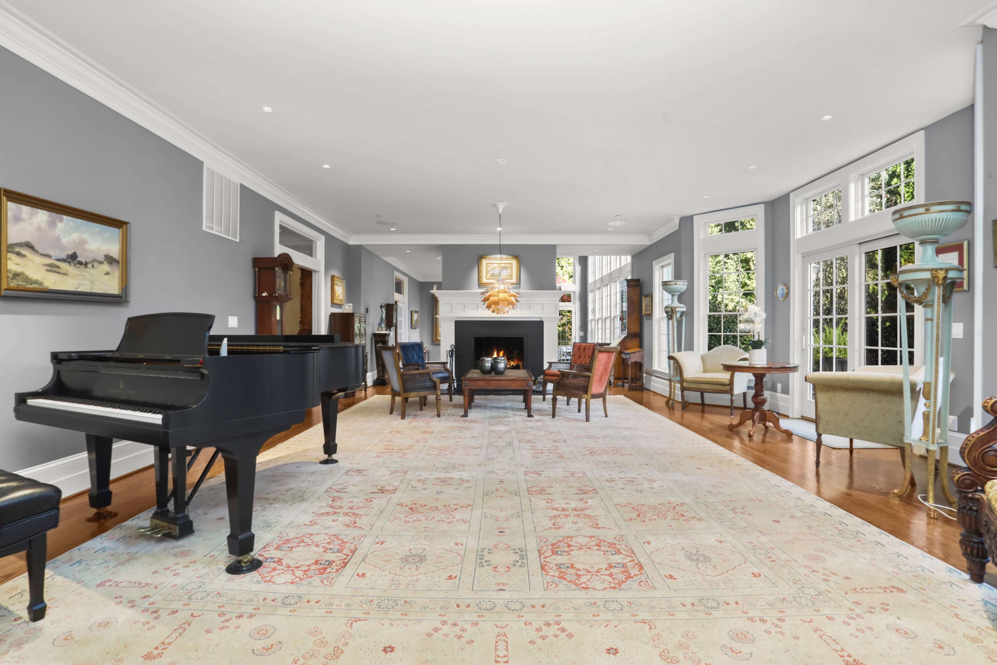 A spacious living room features a grand piano, a central fireplace, and several seating arrangements near large windows.