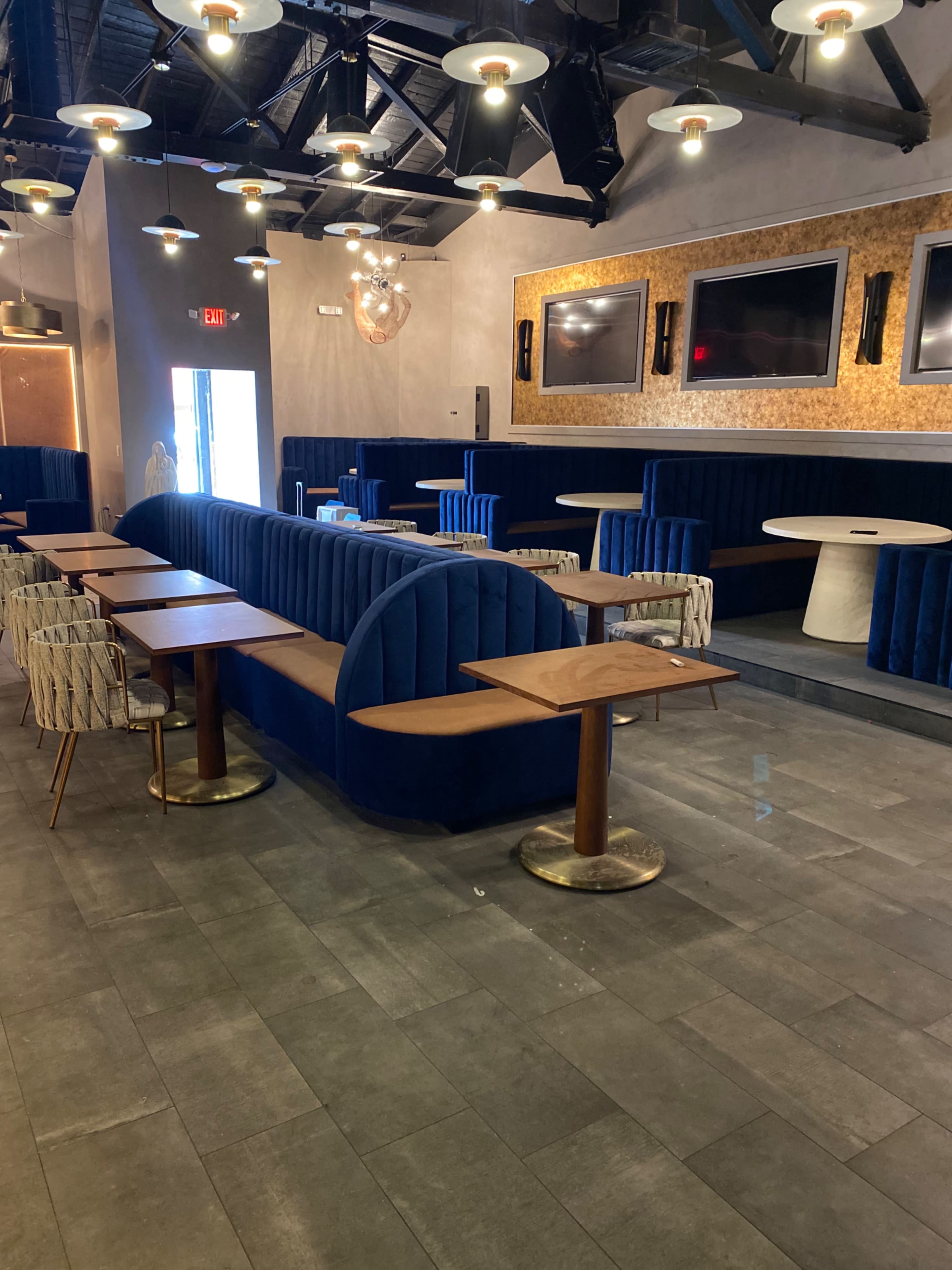 A modern restaurant interior featuring a mix of blue upholstered seating, wooden tables, and pendant lighting.