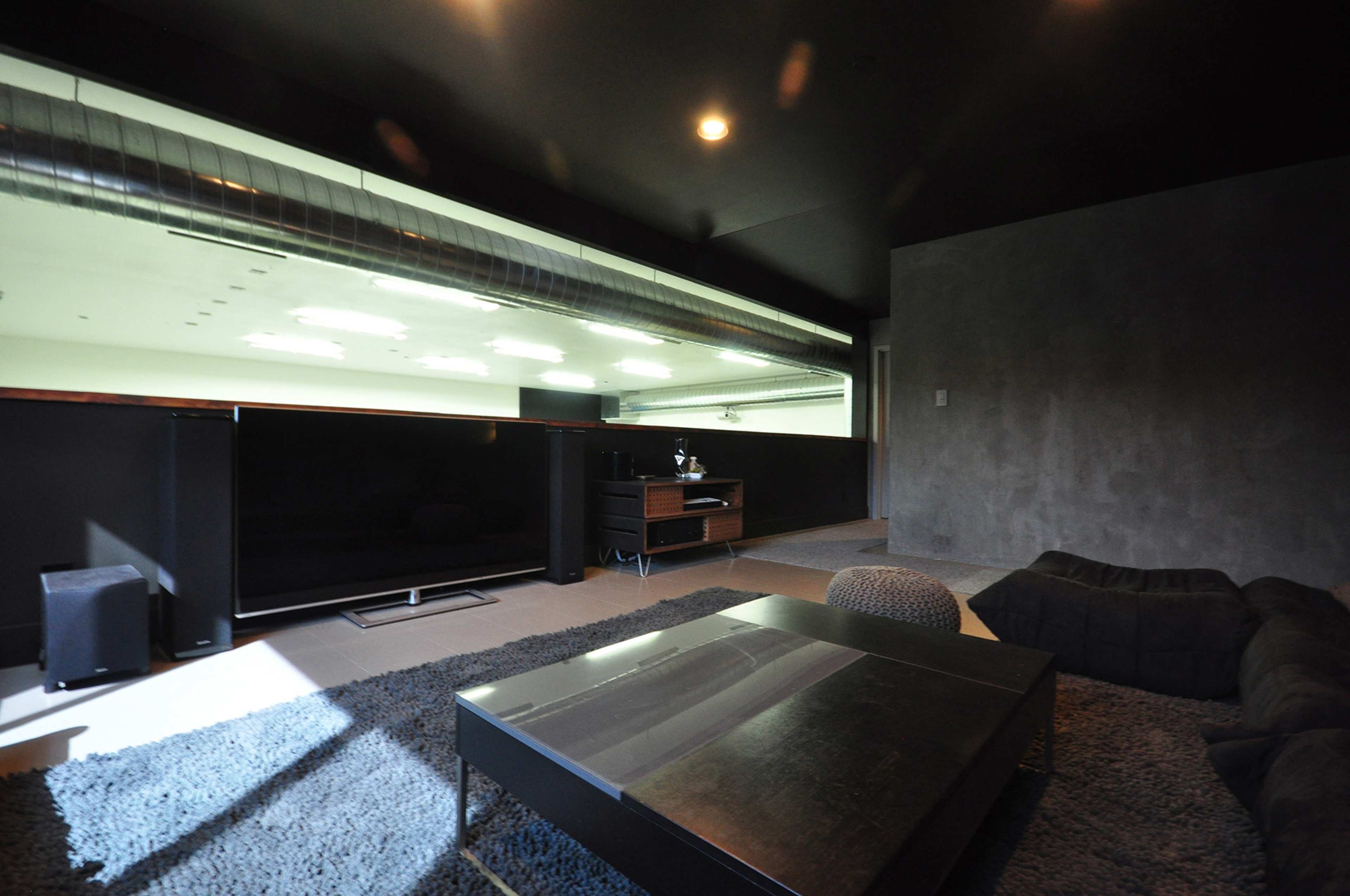 The room features a modern design with a dark color palette, large flat-screen TV, and a plush seating area.