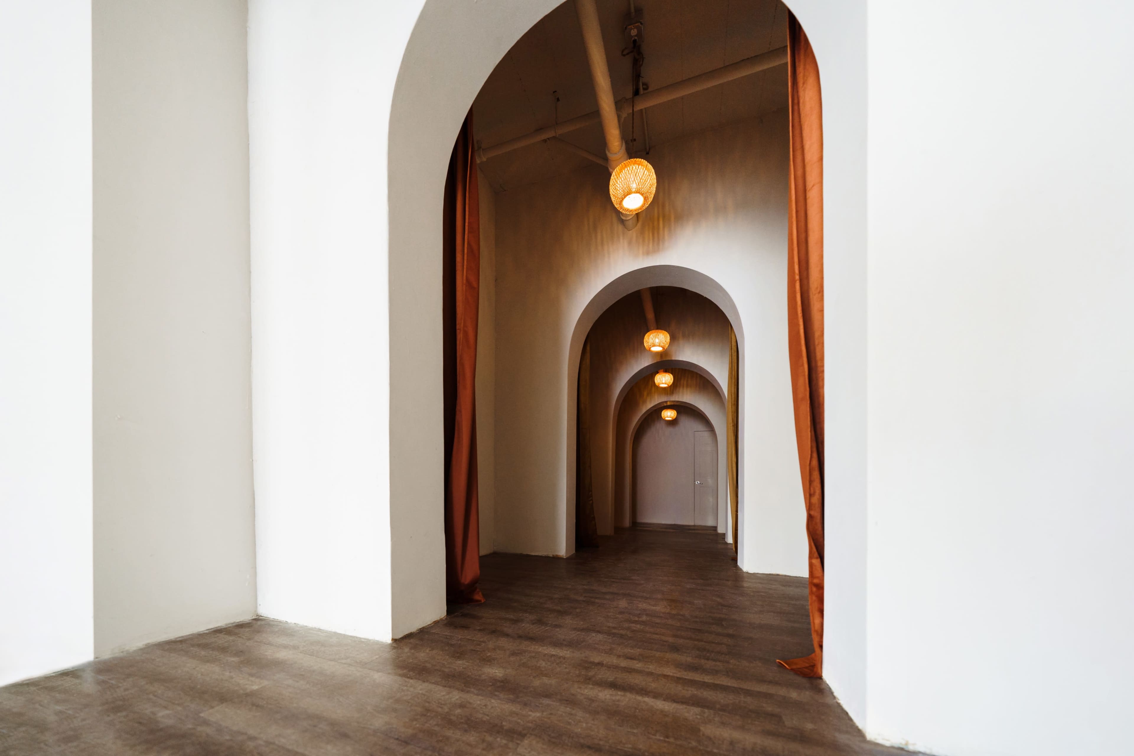 A corridor with archways and pendant lights, featuring orange curtains hanging at the entrances to two side passages.