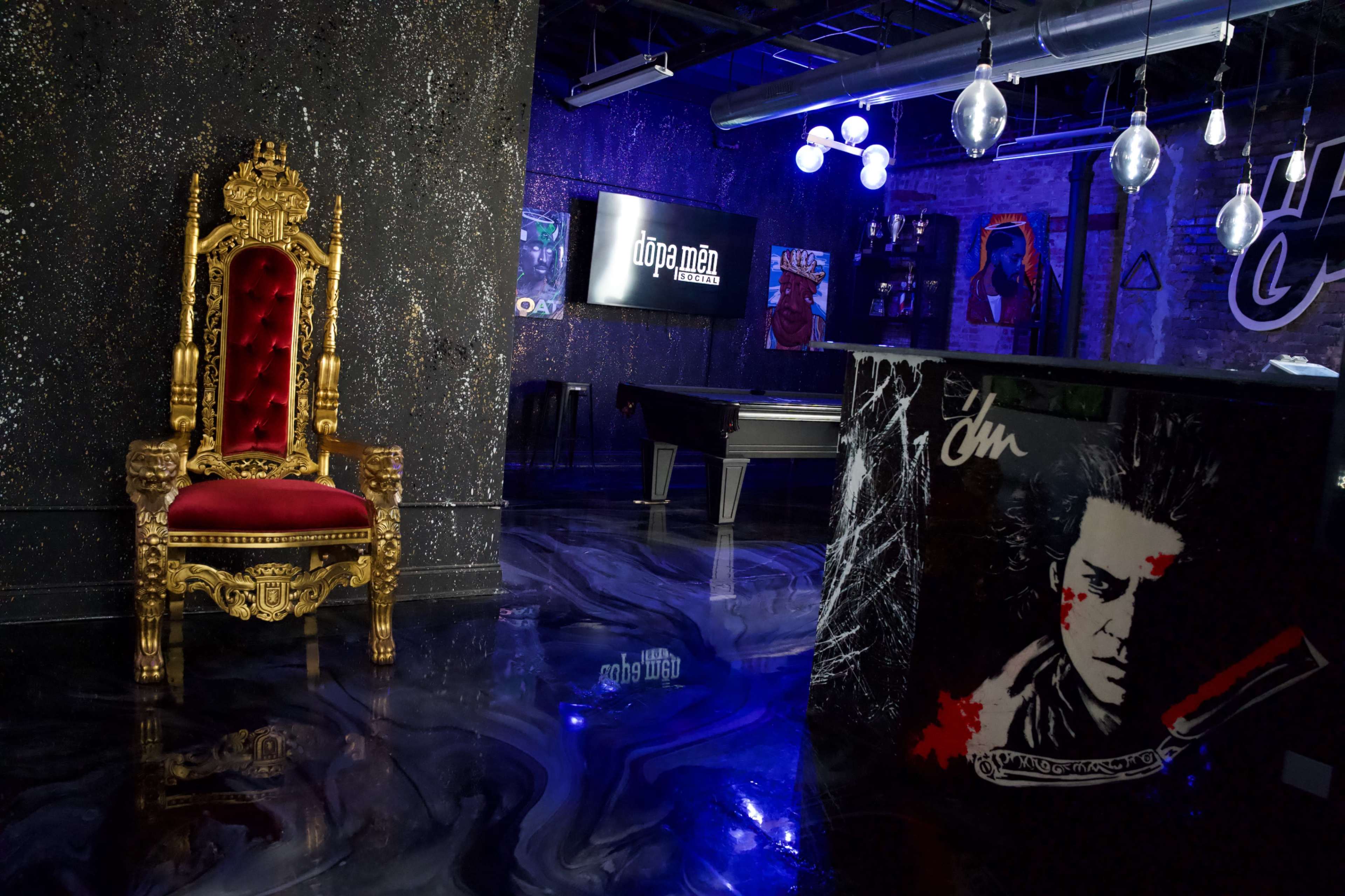 The image shows an opulent golden throne with red velvet upholstery against a backdrop of dark, glossy flooring and modern decor, featuring artwork and a pool table.