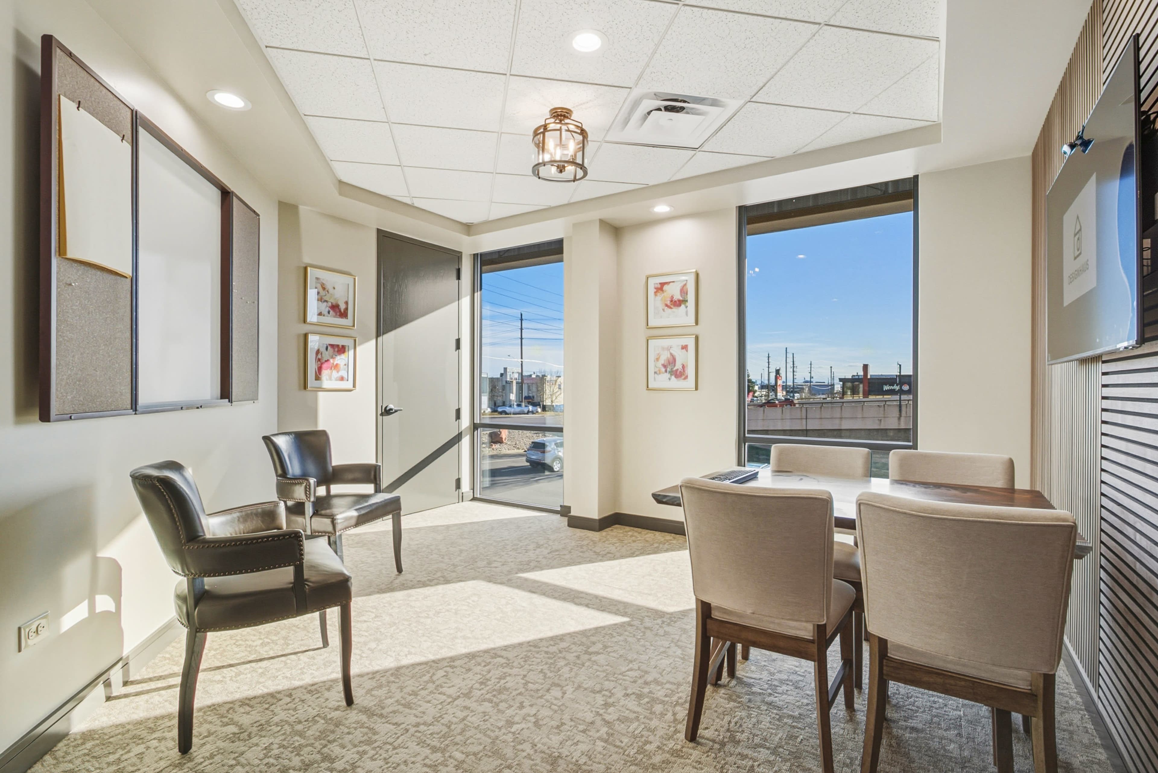 The image shows a modern meeting room featuring two chairs, a table, and large windows that provide a view of an outdoor area.