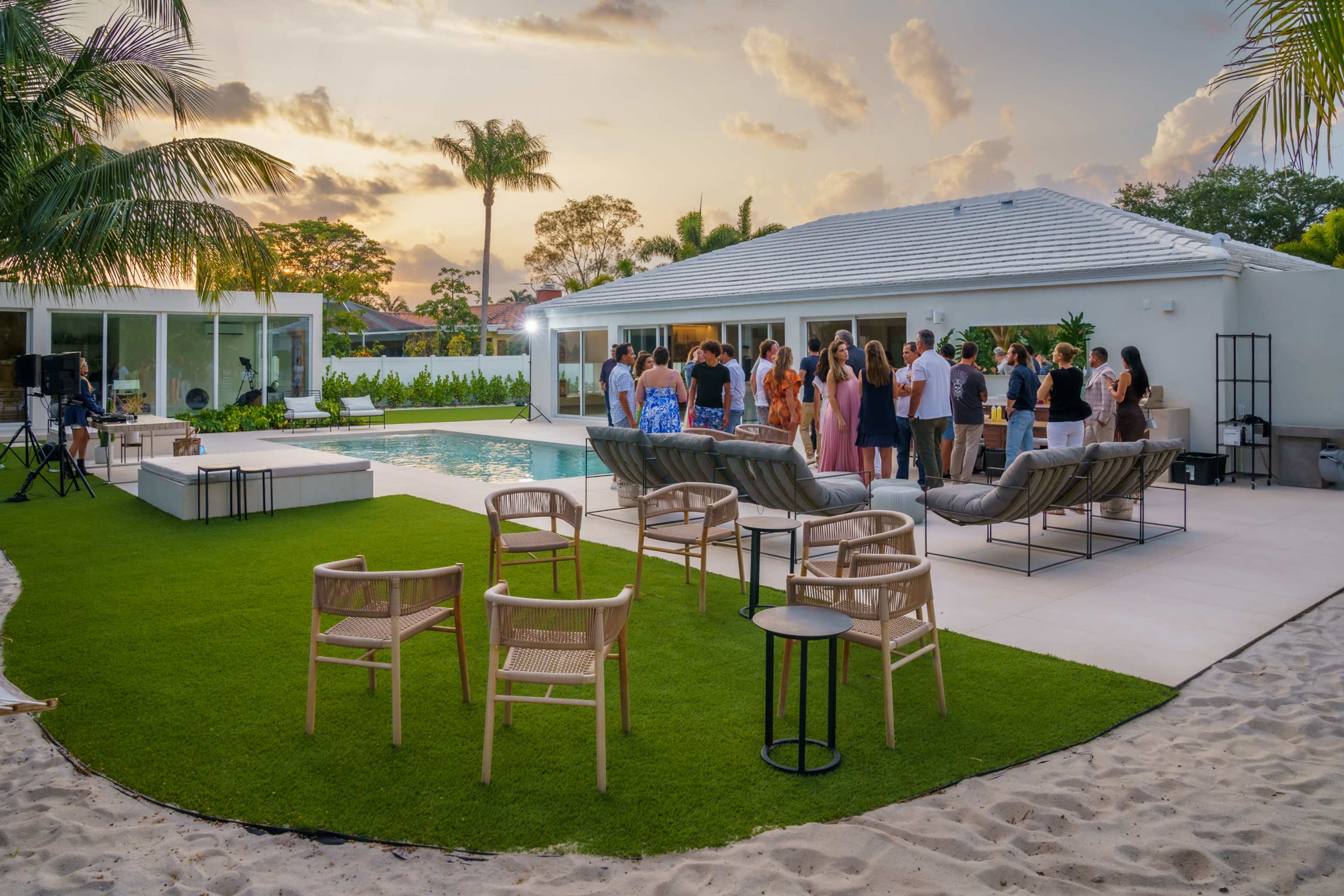 A group of people socializes around a swimming pool in a backyard setting during sunset.