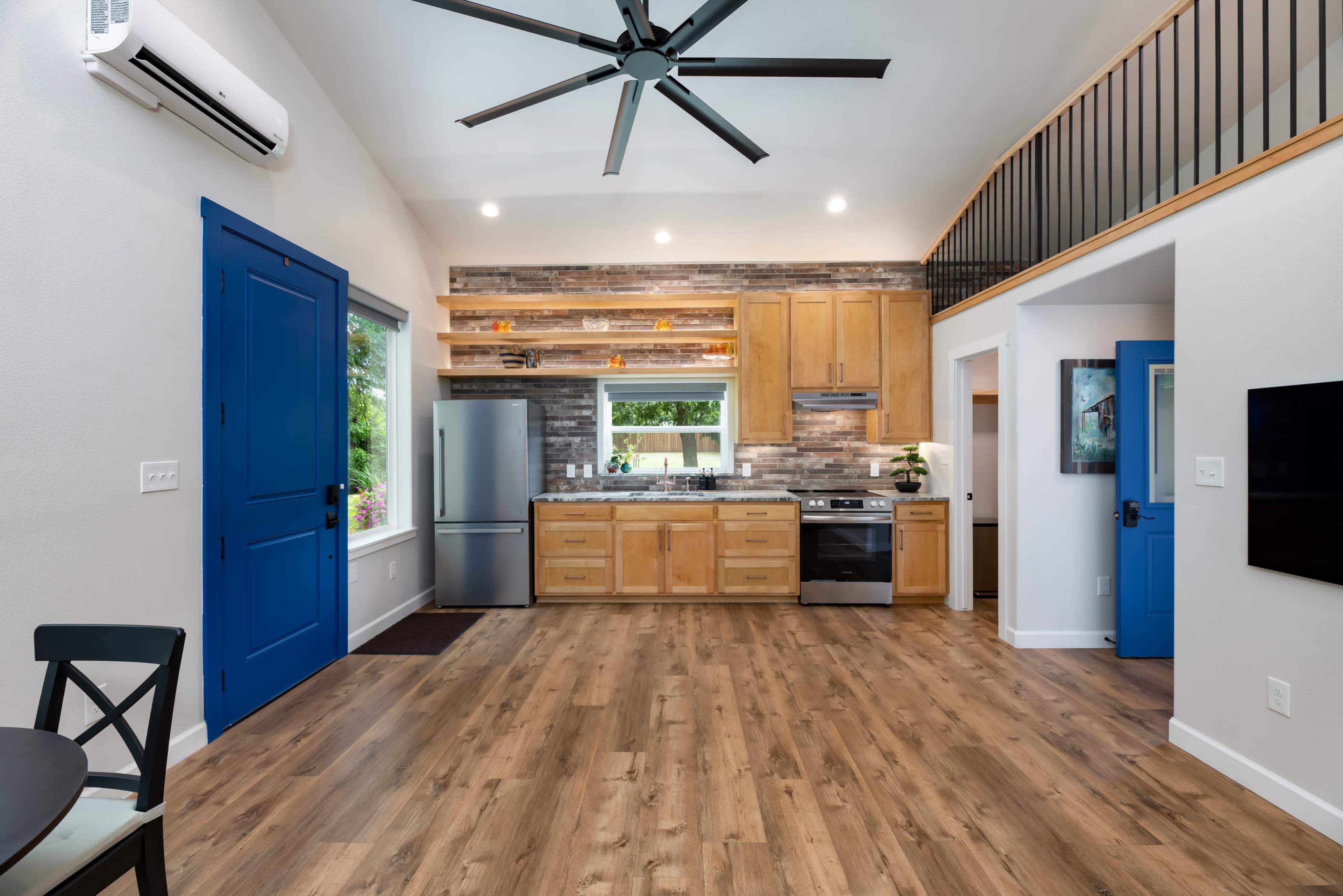 The image shows a modern kitchen and dining area with wooden cabinets, a stainless steel refrigerator, and bright blue doors.