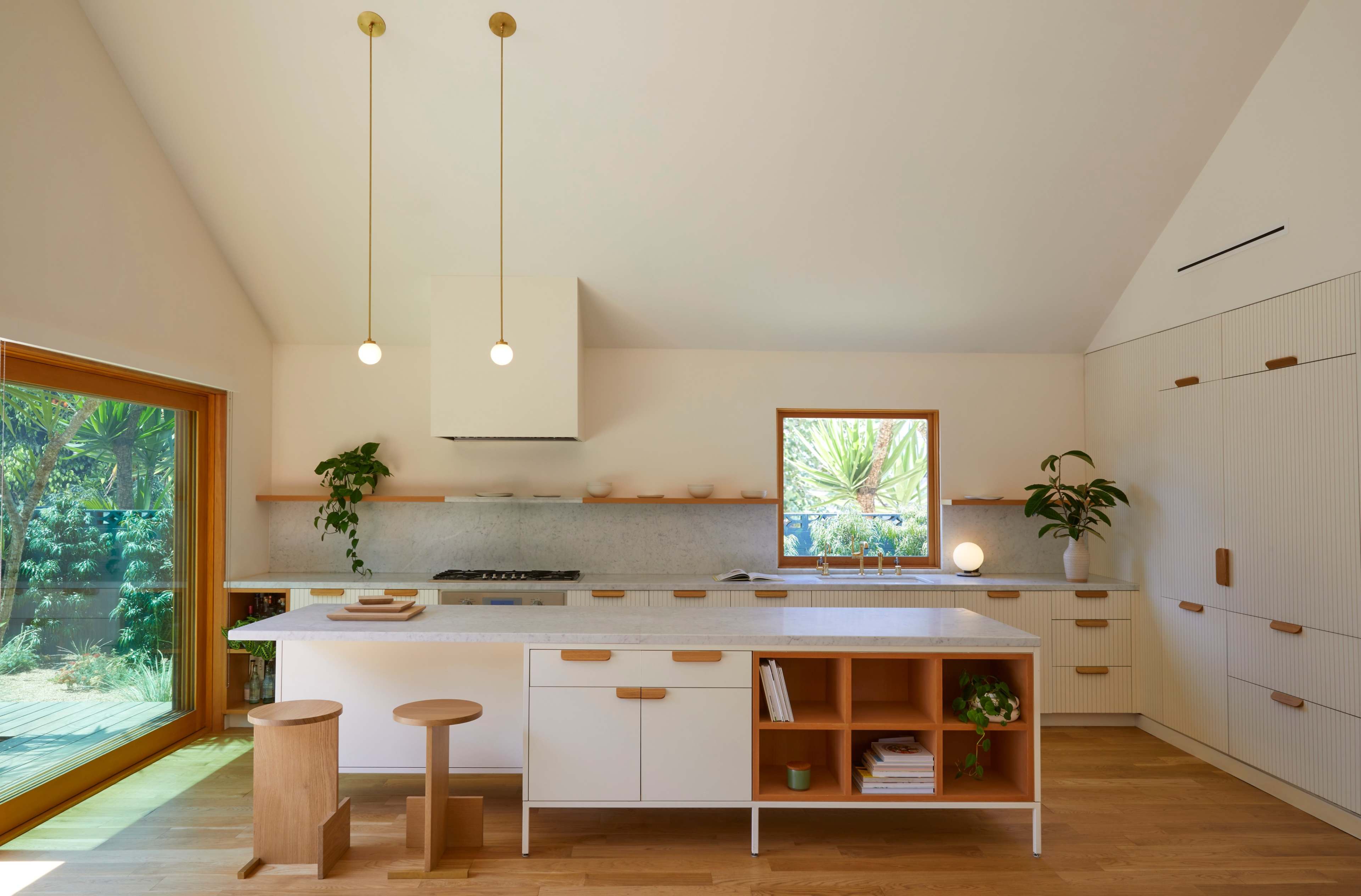 A modern kitchen features a central island with stools, white cabinetry, and large windows that provide natural light.
