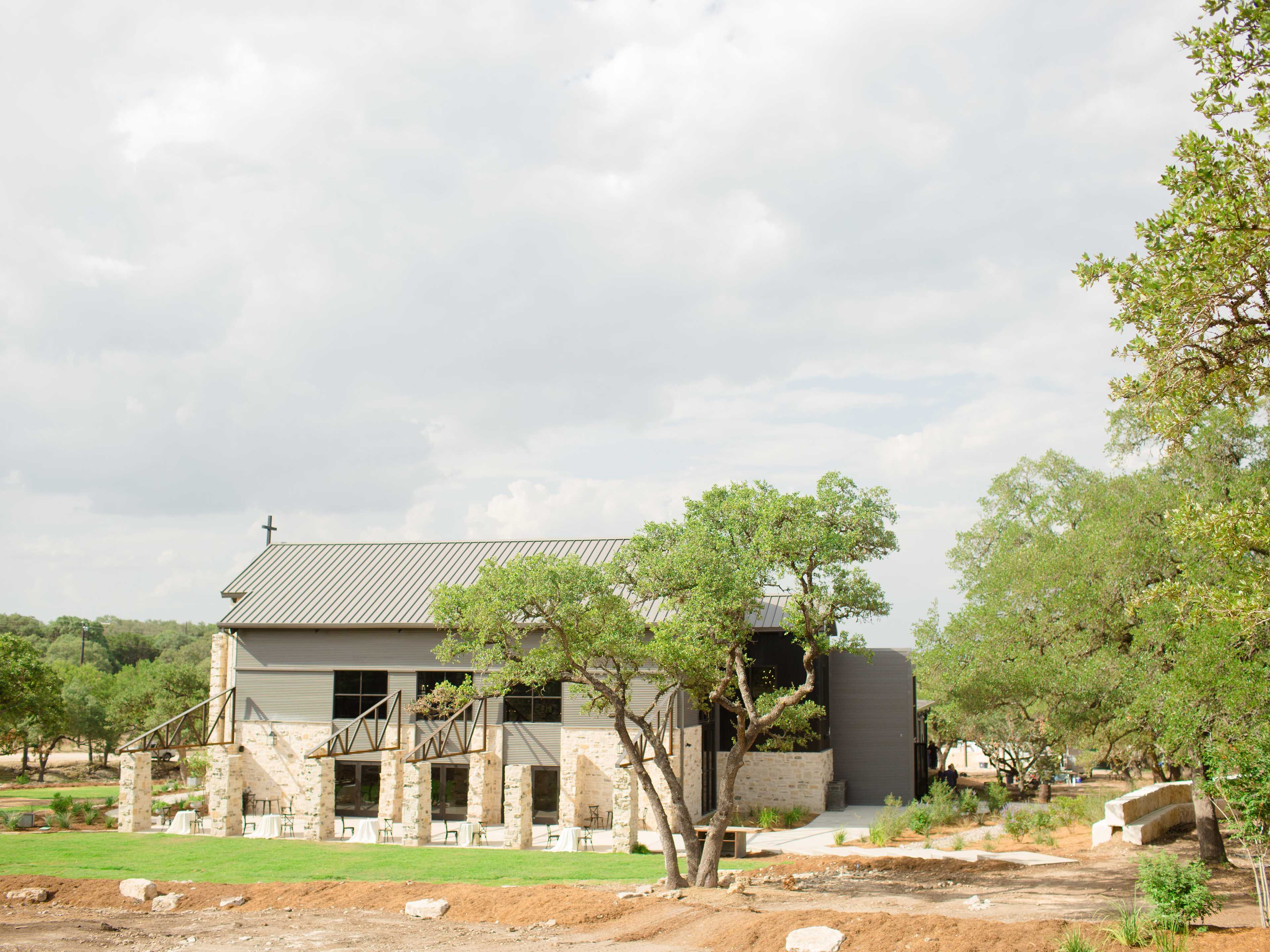 A modern building with a stone foundation and metal roof stands among trees in a natural setting.
