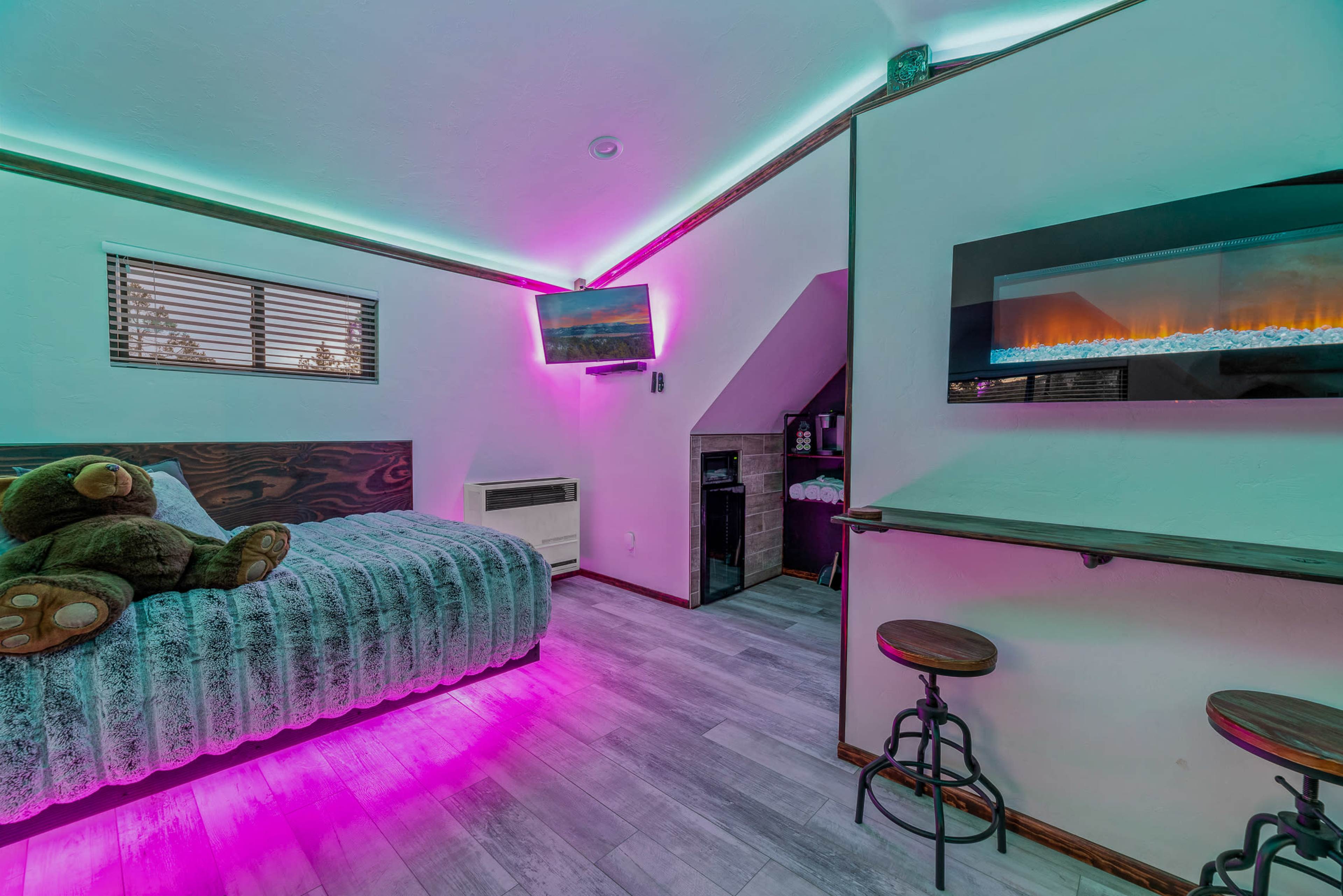 A modern bedroom with a bed, a television mounted on the wall, and ambient lighting that creates a colorful atmosphere.