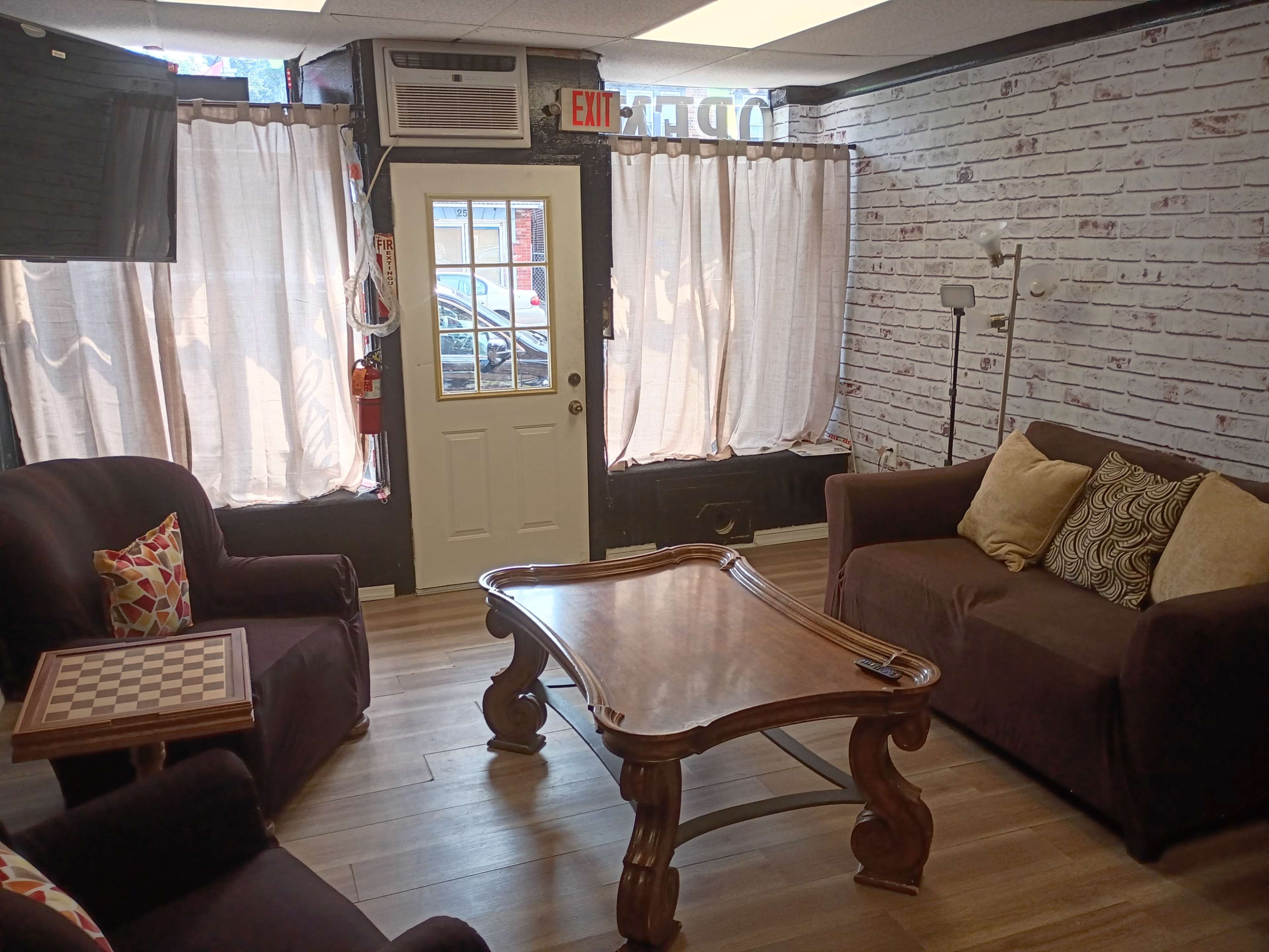 The image shows a cozy seating area with two brown sofas, a wooden coffee table, and light curtains covering the windows.