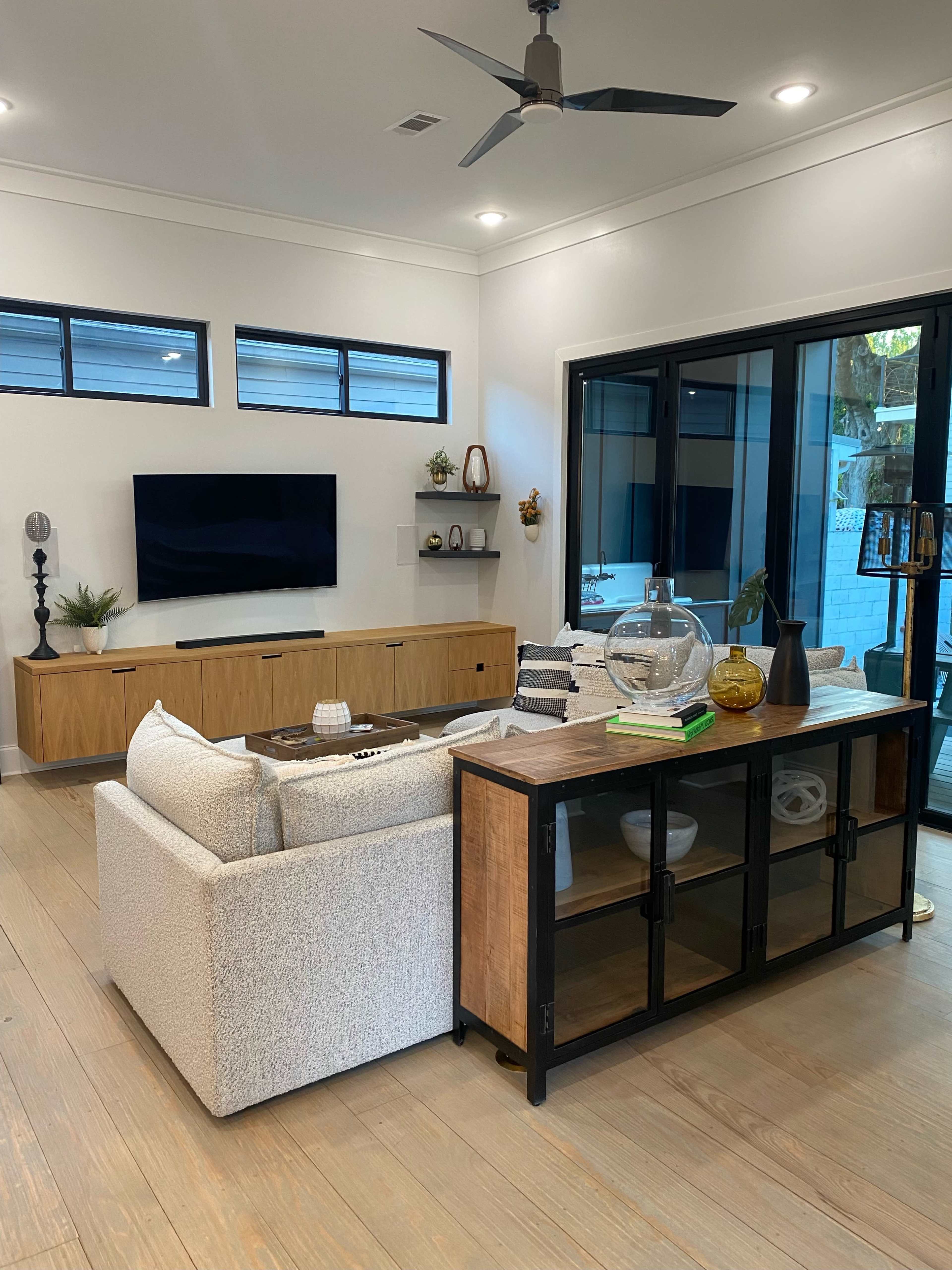 A modern living room with a white sofa, a wooden sideboard, and large windows that provide natural light.