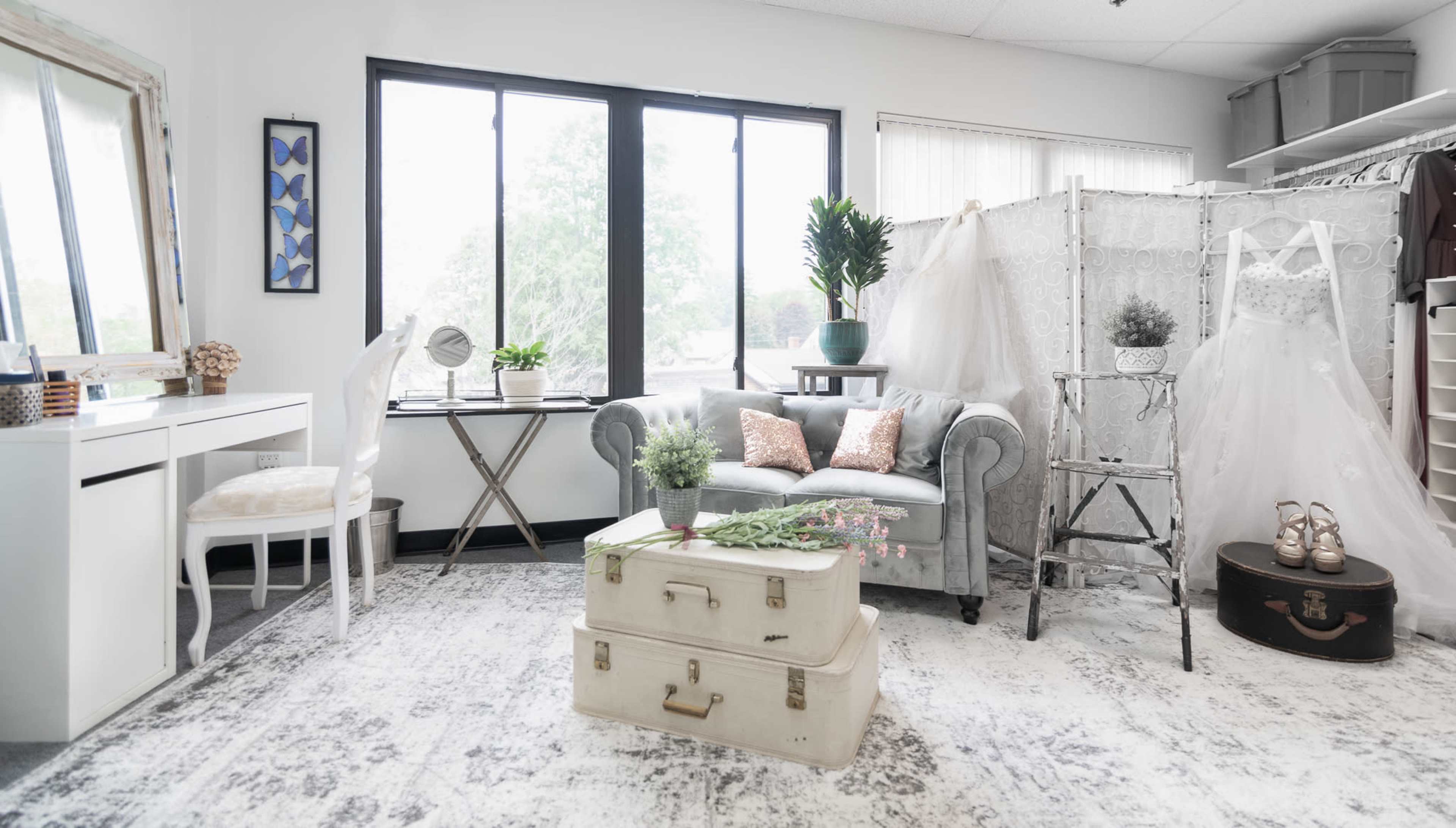 A well-organized, light-filled interior space with a sofa, various plants, and wedding attire on display.
