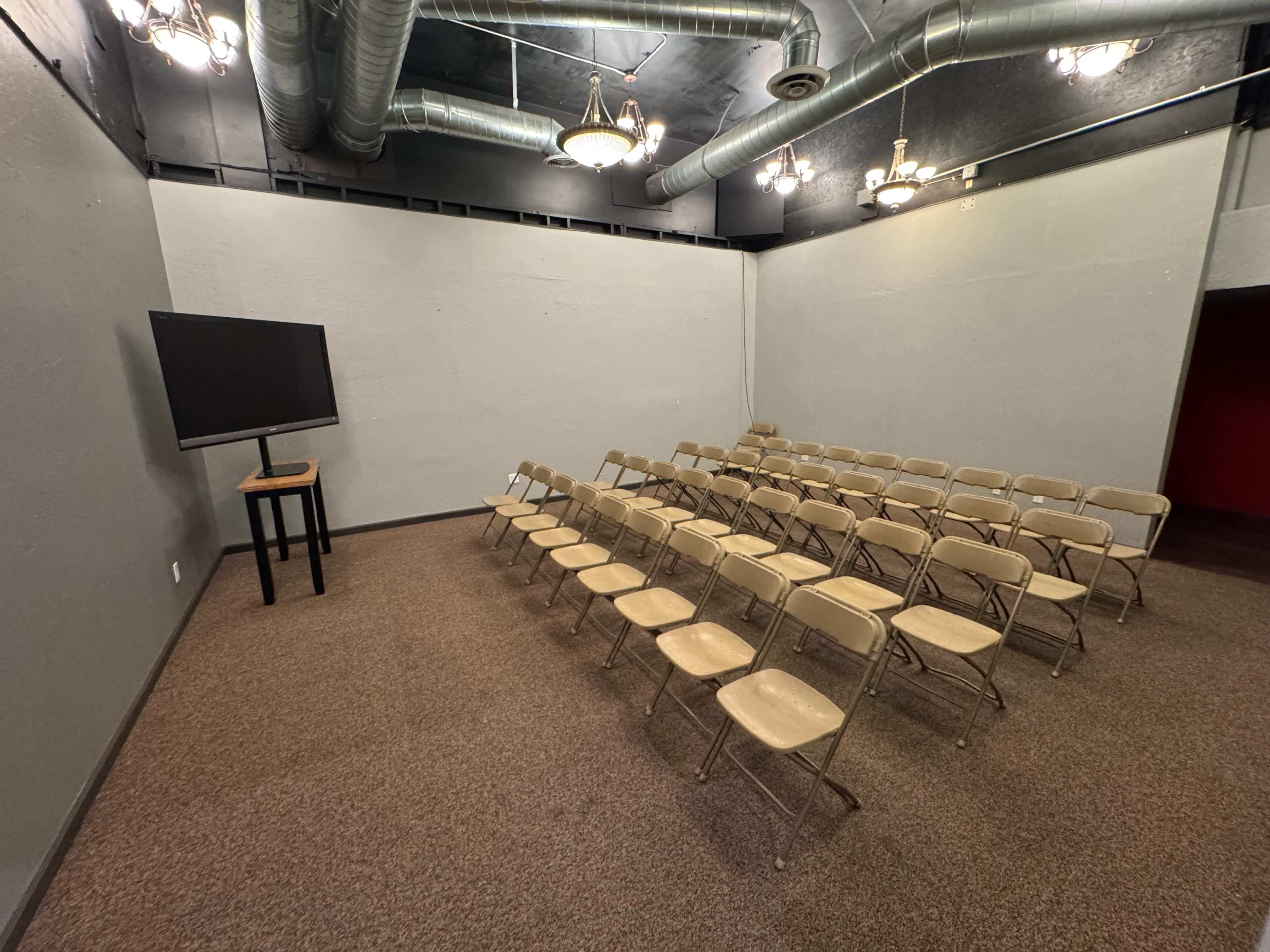 The image shows a small, empty room configured with rows of folding chairs facing a television on a stand.