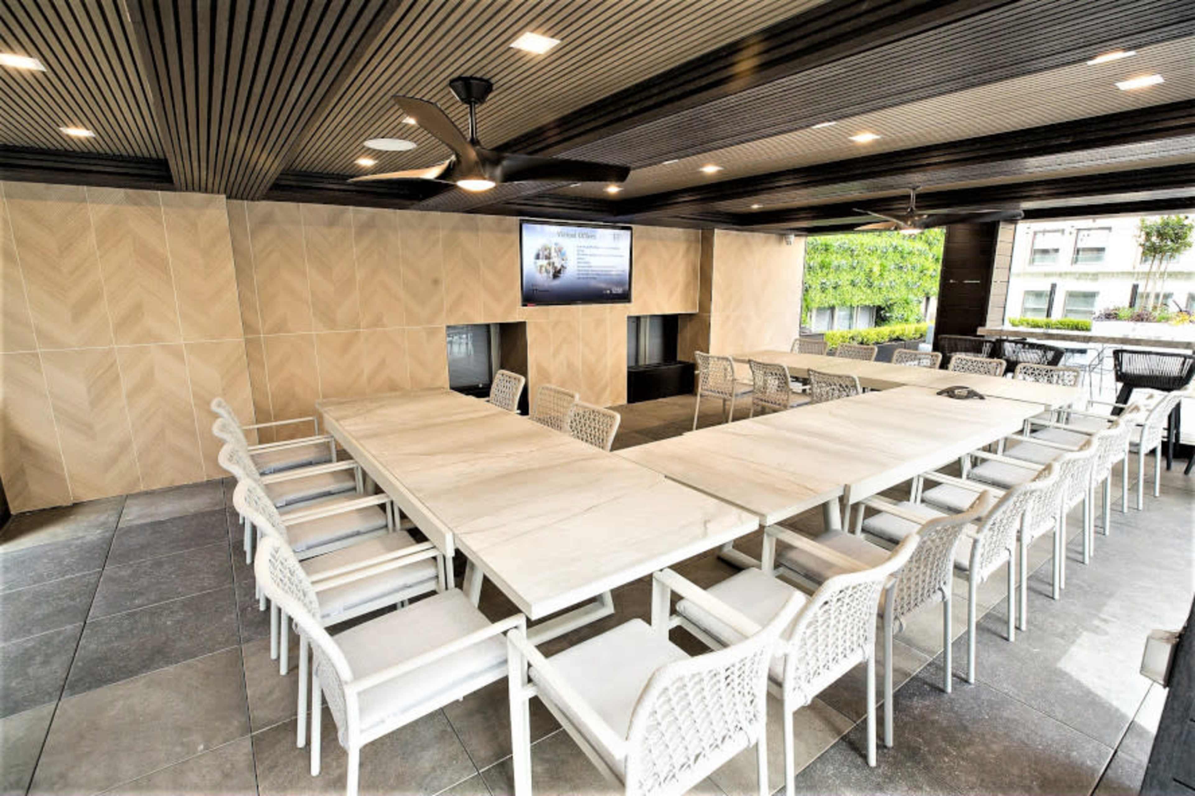 A large, modern meeting room features a long table surrounded by white chairs, with a screen displaying information on a wall.