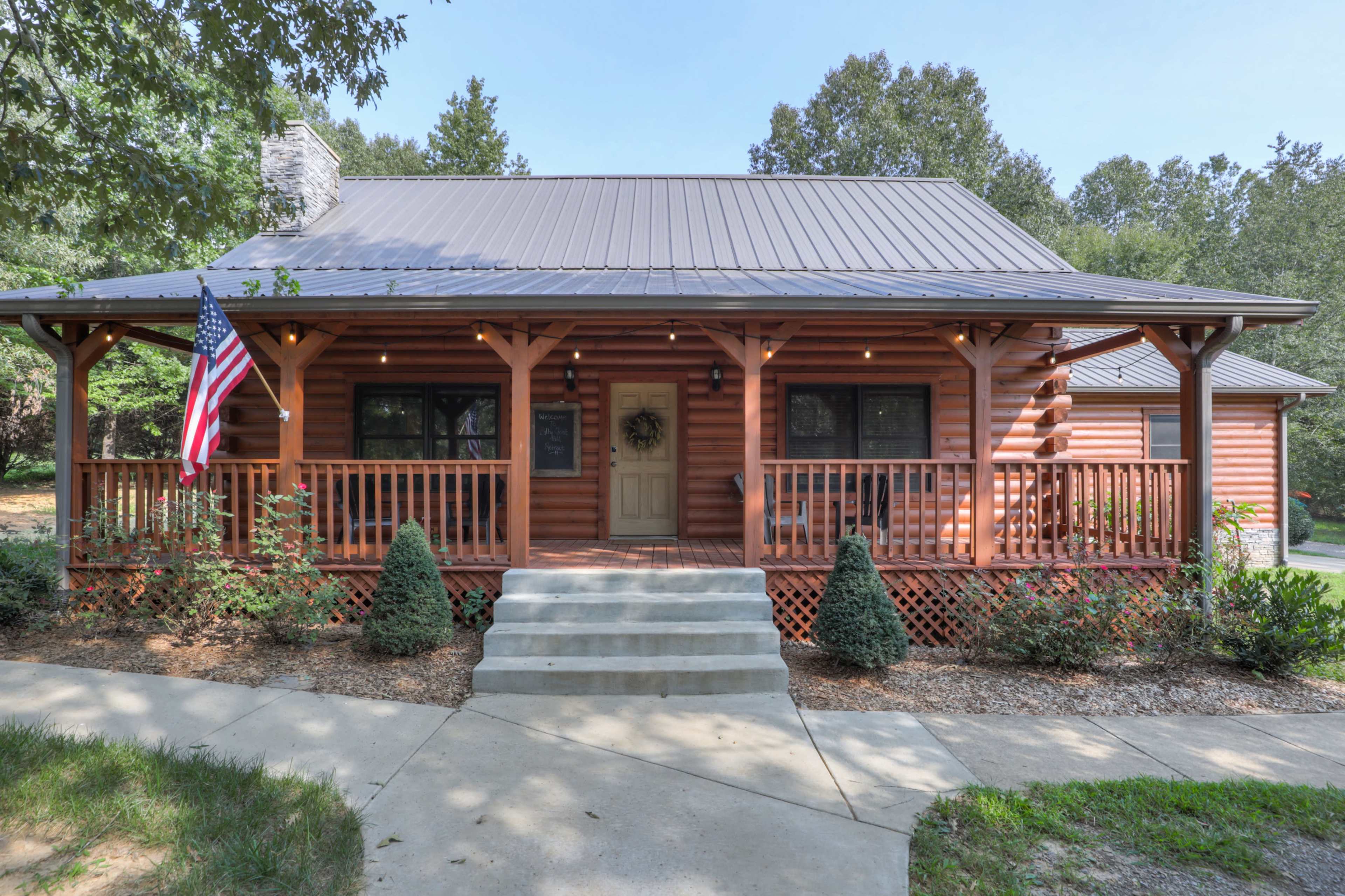 A log cabin with a front porch, steps leading to the door, and an American flag displayed prominently.