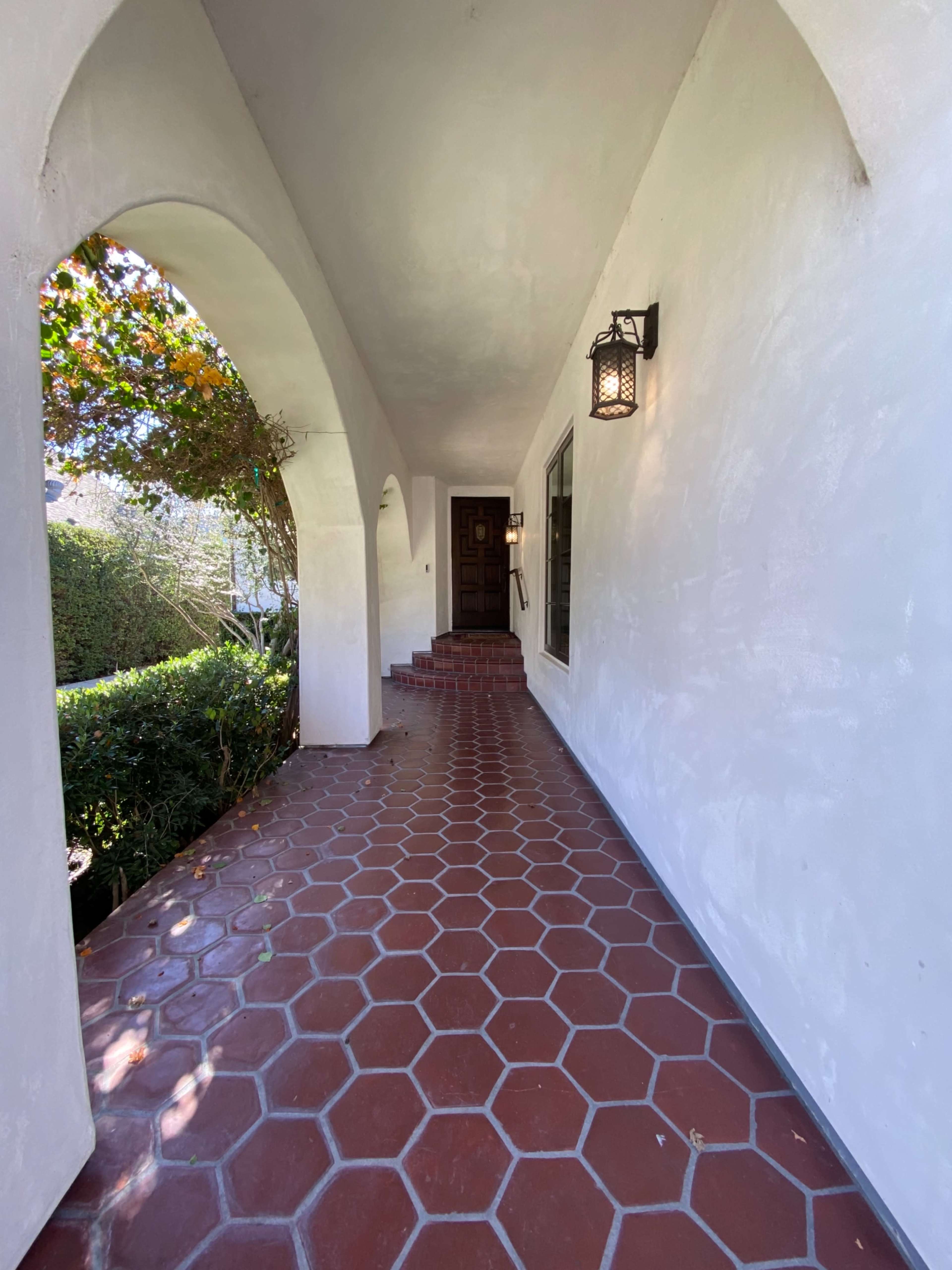 A hallway with a tiled floor, arched openings, and a staircase leading to a front door under a lantern.