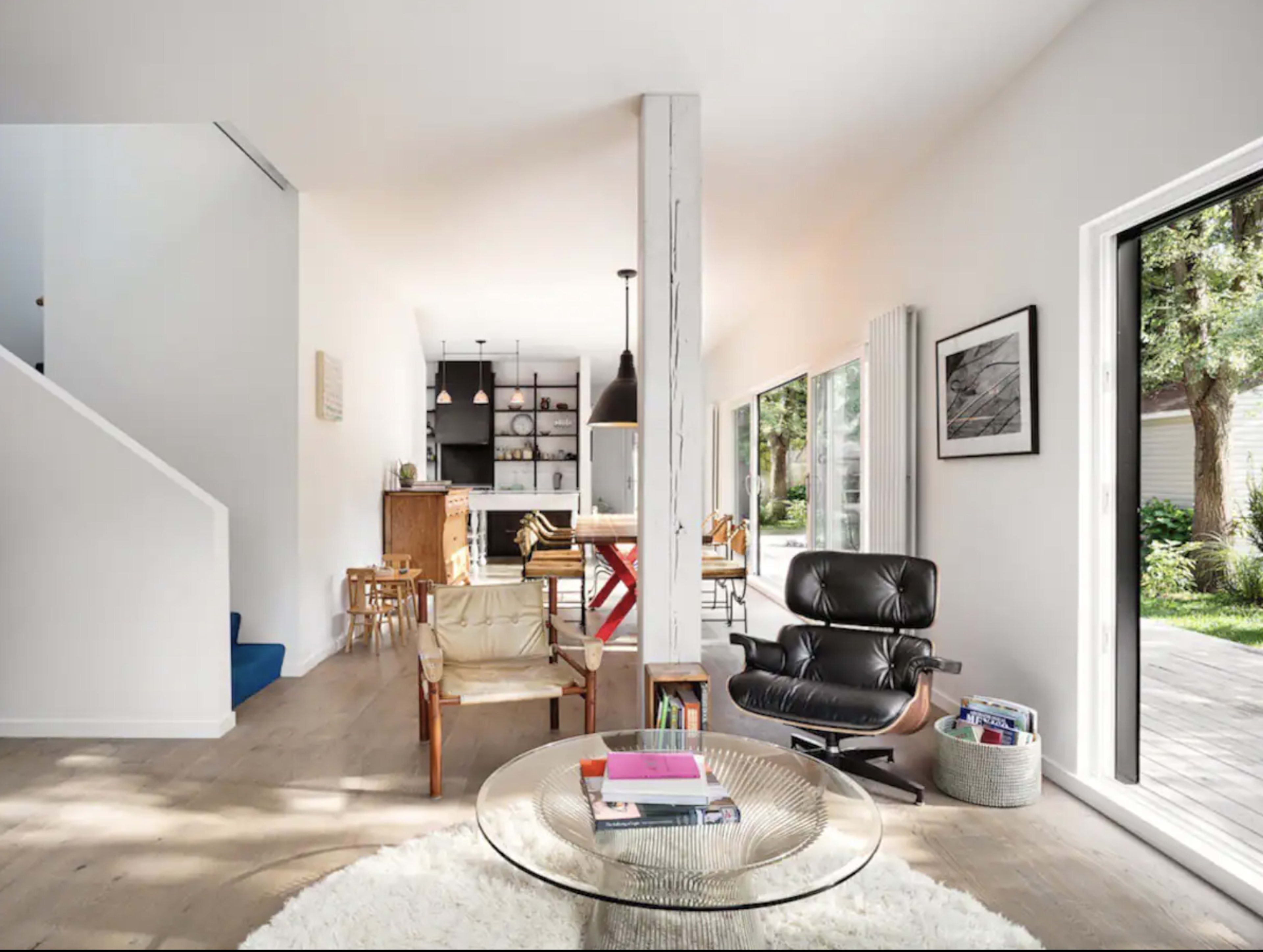 A modern living space with a seating area, dining area, and large windows overlooking a backyard.