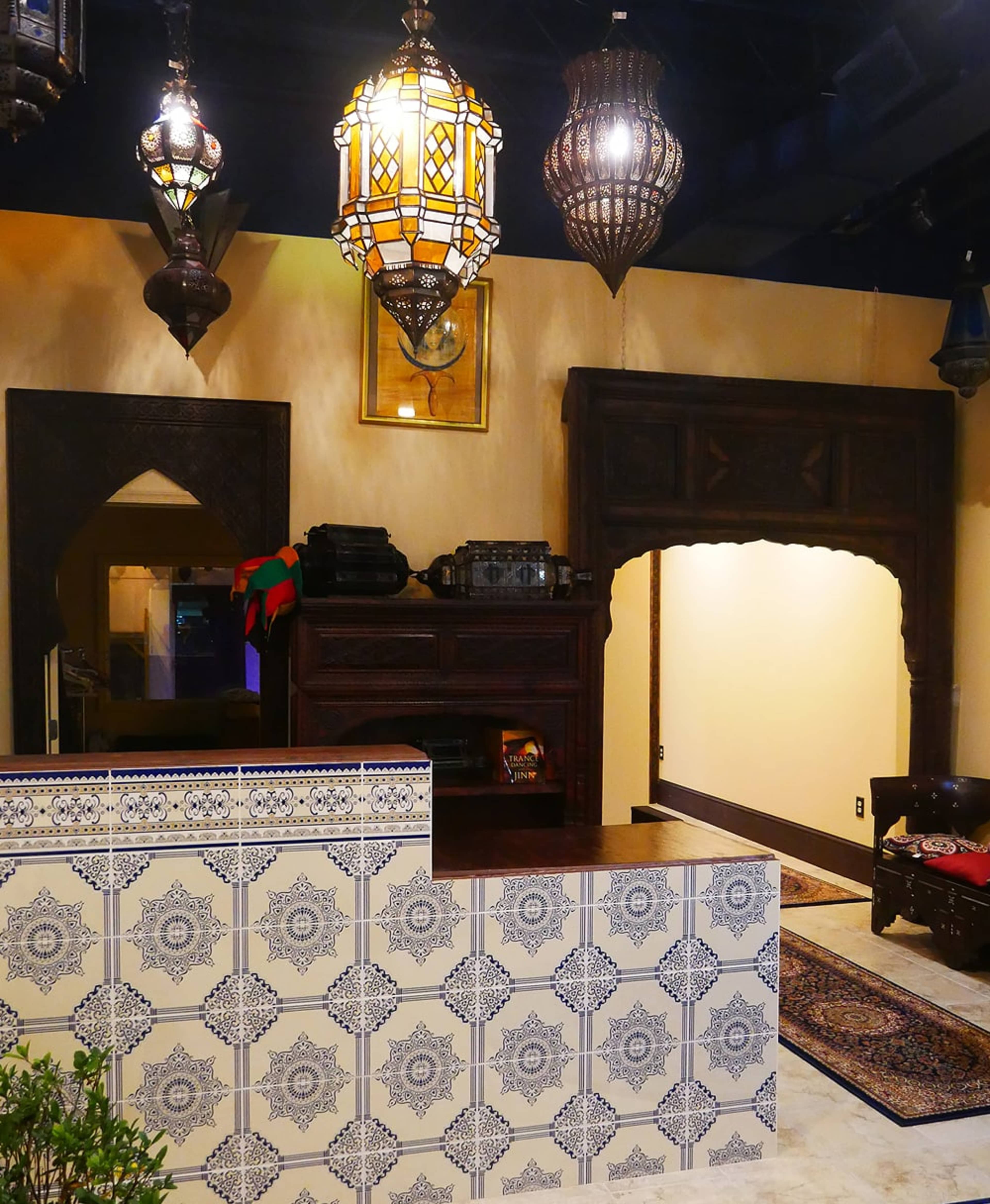 The interior of a Moroccan-style reception area features ornate light fixtures, intricate tile work, and an arched doorway leading to another room.