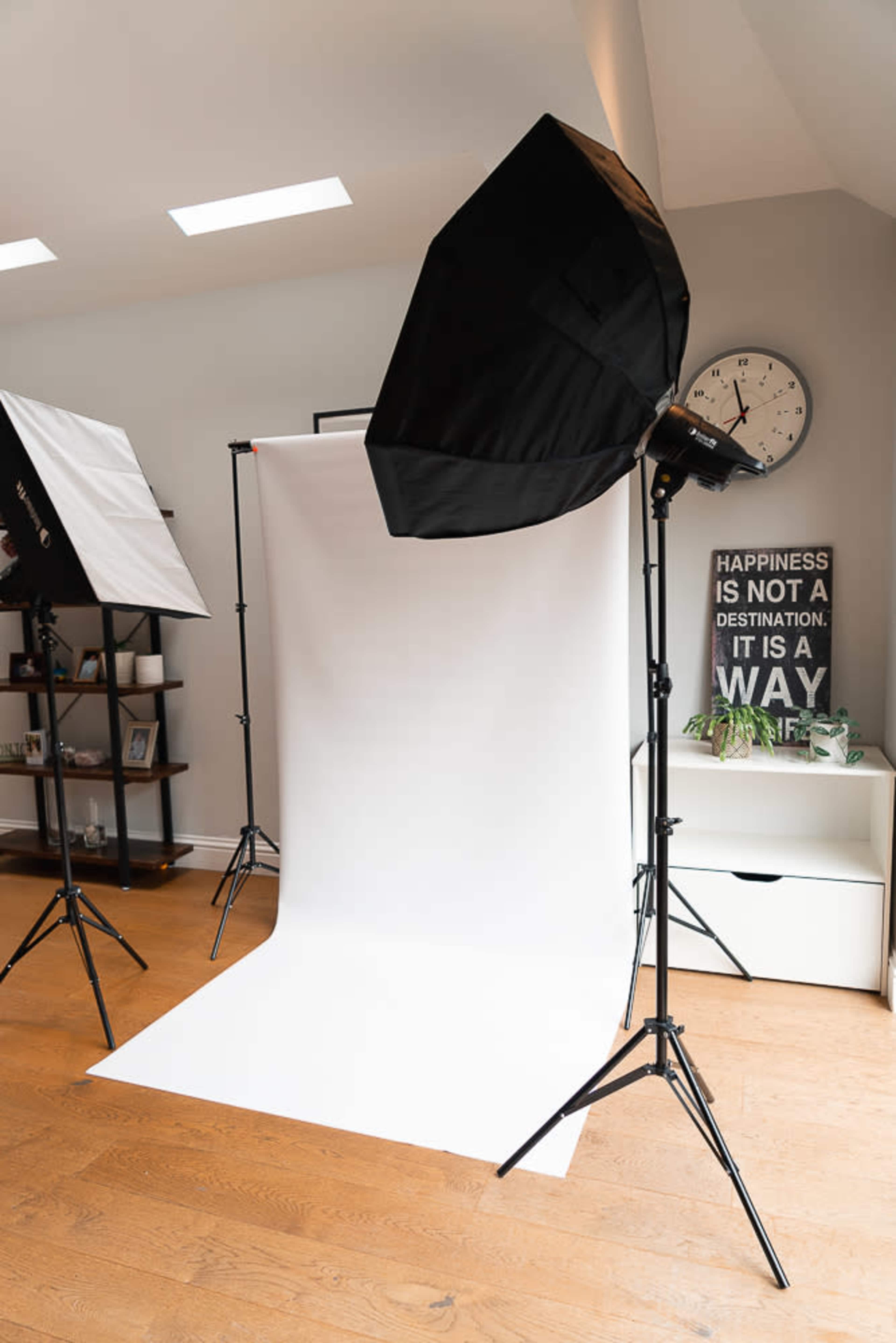 A photography studio setup with two light stands and a white backdrop in a well-lit room.