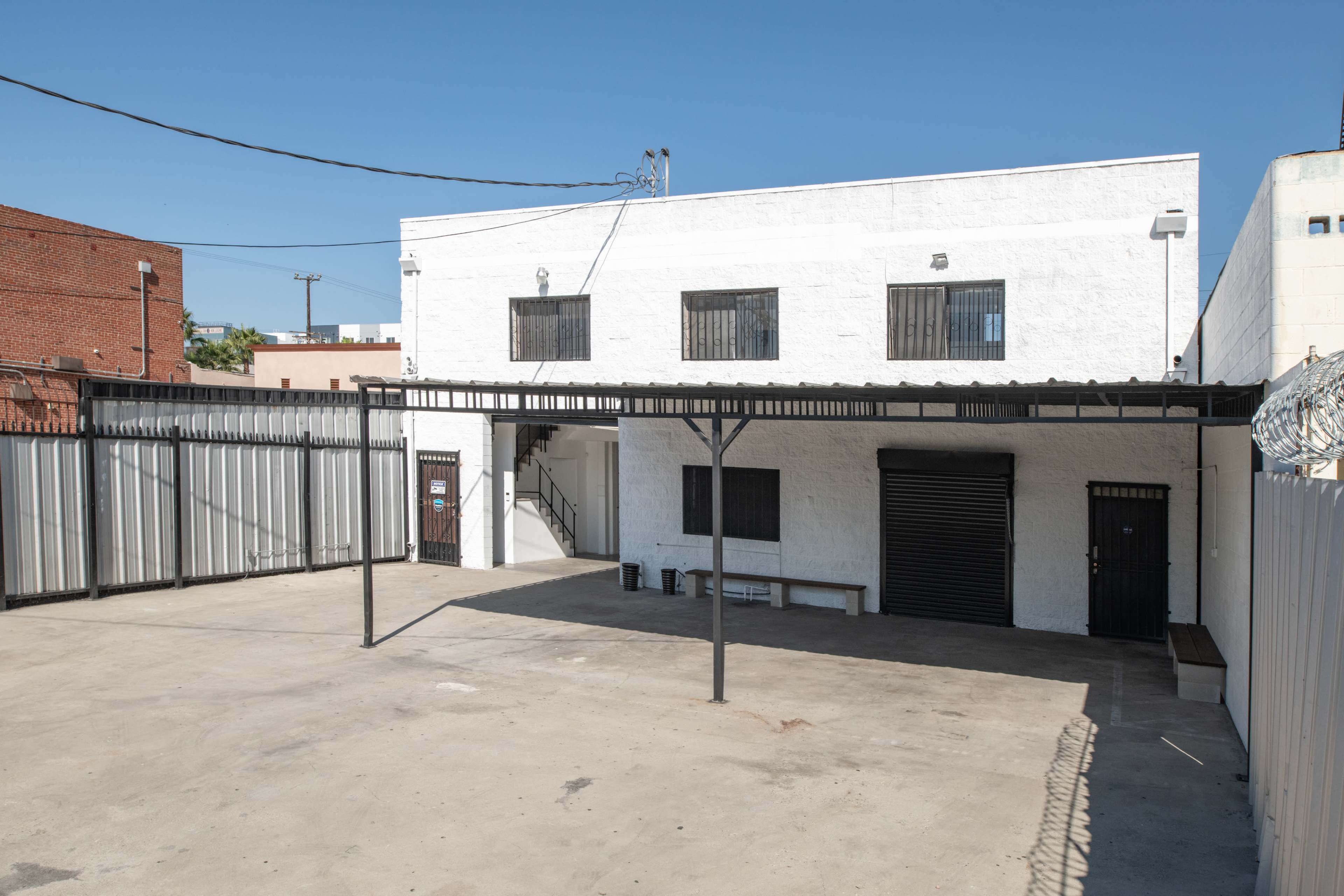 A white two-story building with barred windows surrounded by a concrete lot and a metal canopy.