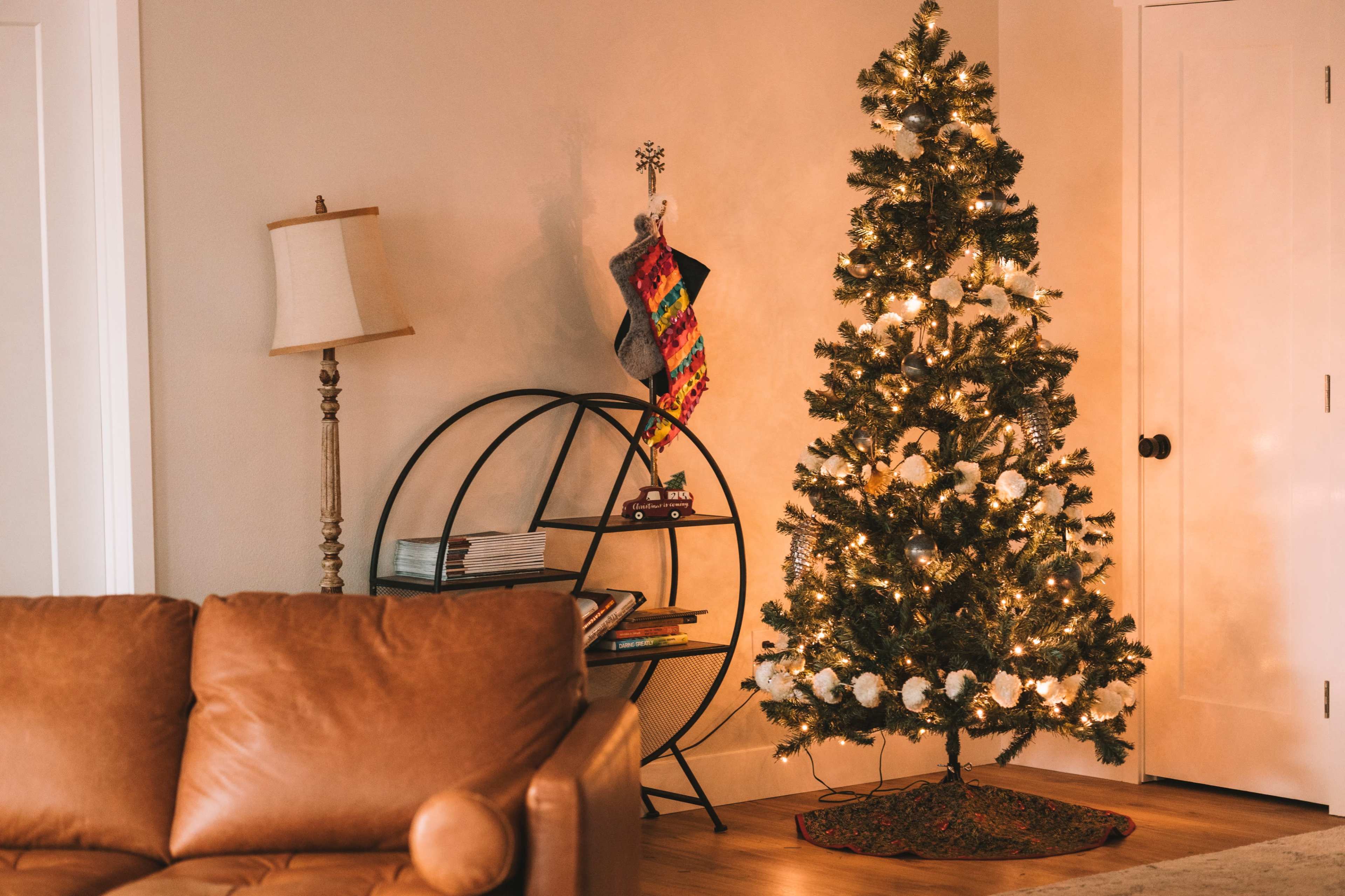 A decorated Christmas tree with lights and ornaments stands next to a bookshelf, while a cozy brown couch is positioned nearby.