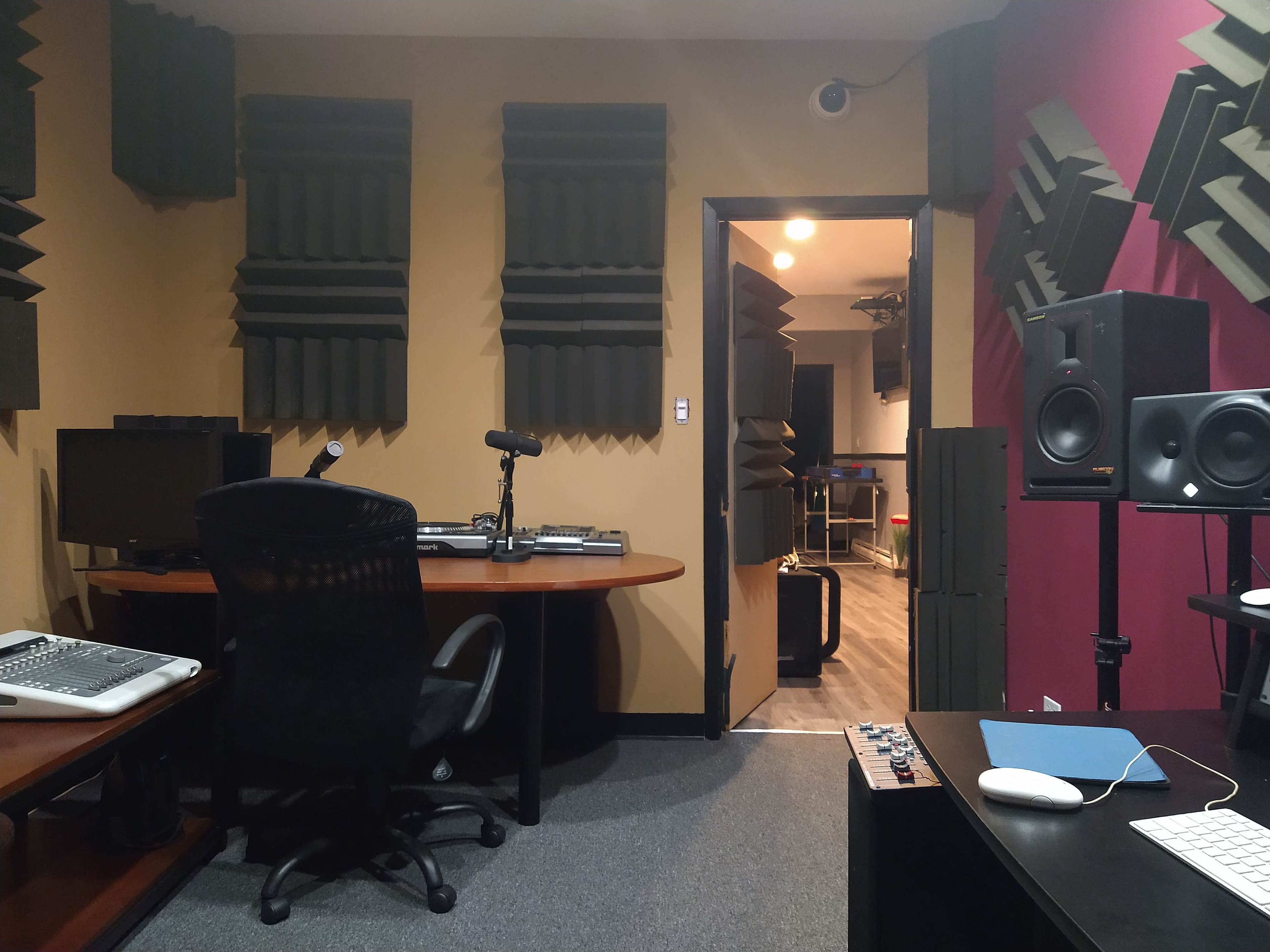 A soundproof recording studio featuring acoustic panels on the walls, a desk with audio equipment, and a doorway leading to another room.