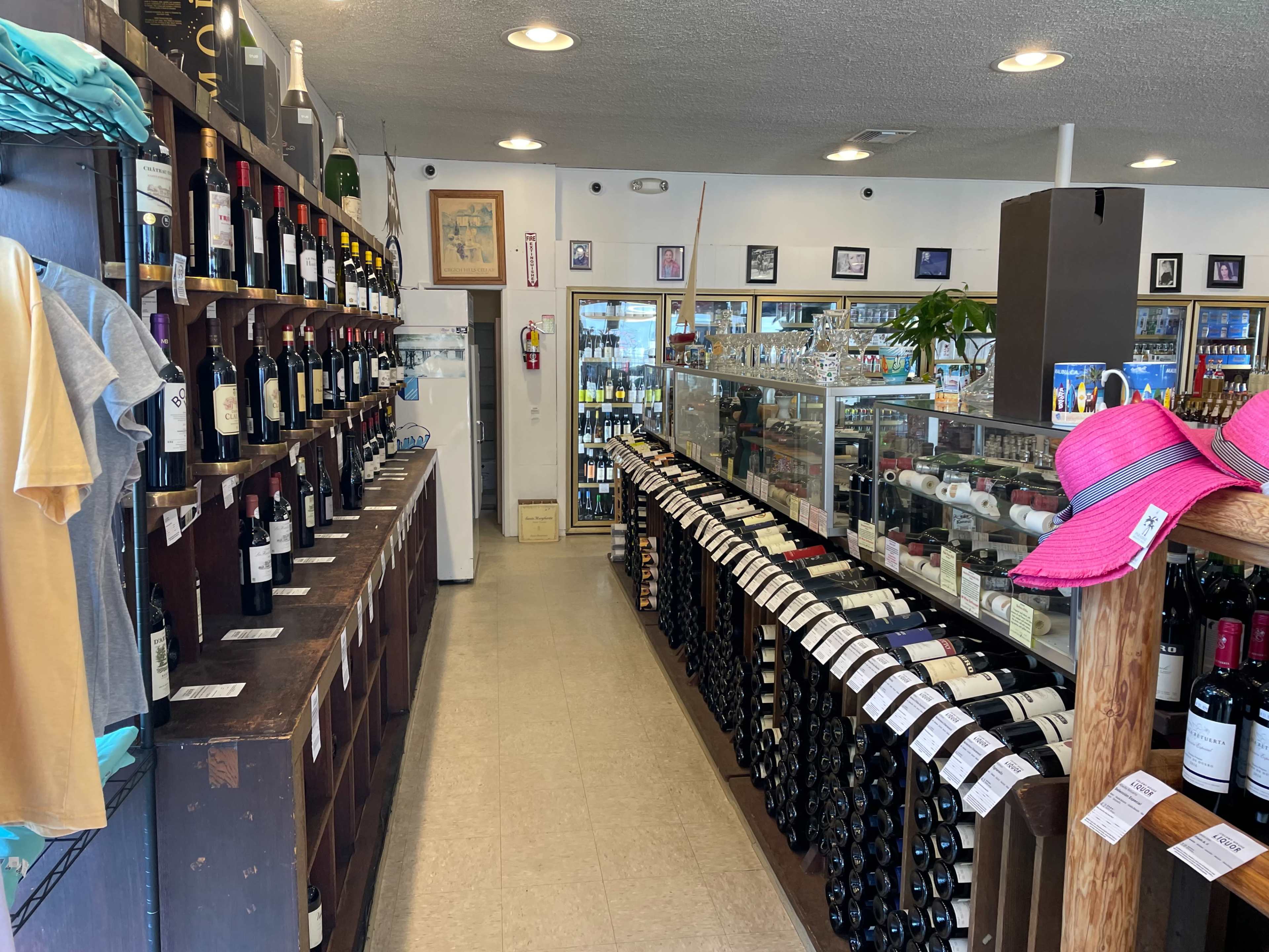 The interior of a wine shop features shelves lined with various bottles of wine on both sides, and a display counter at the back with additional offerings.