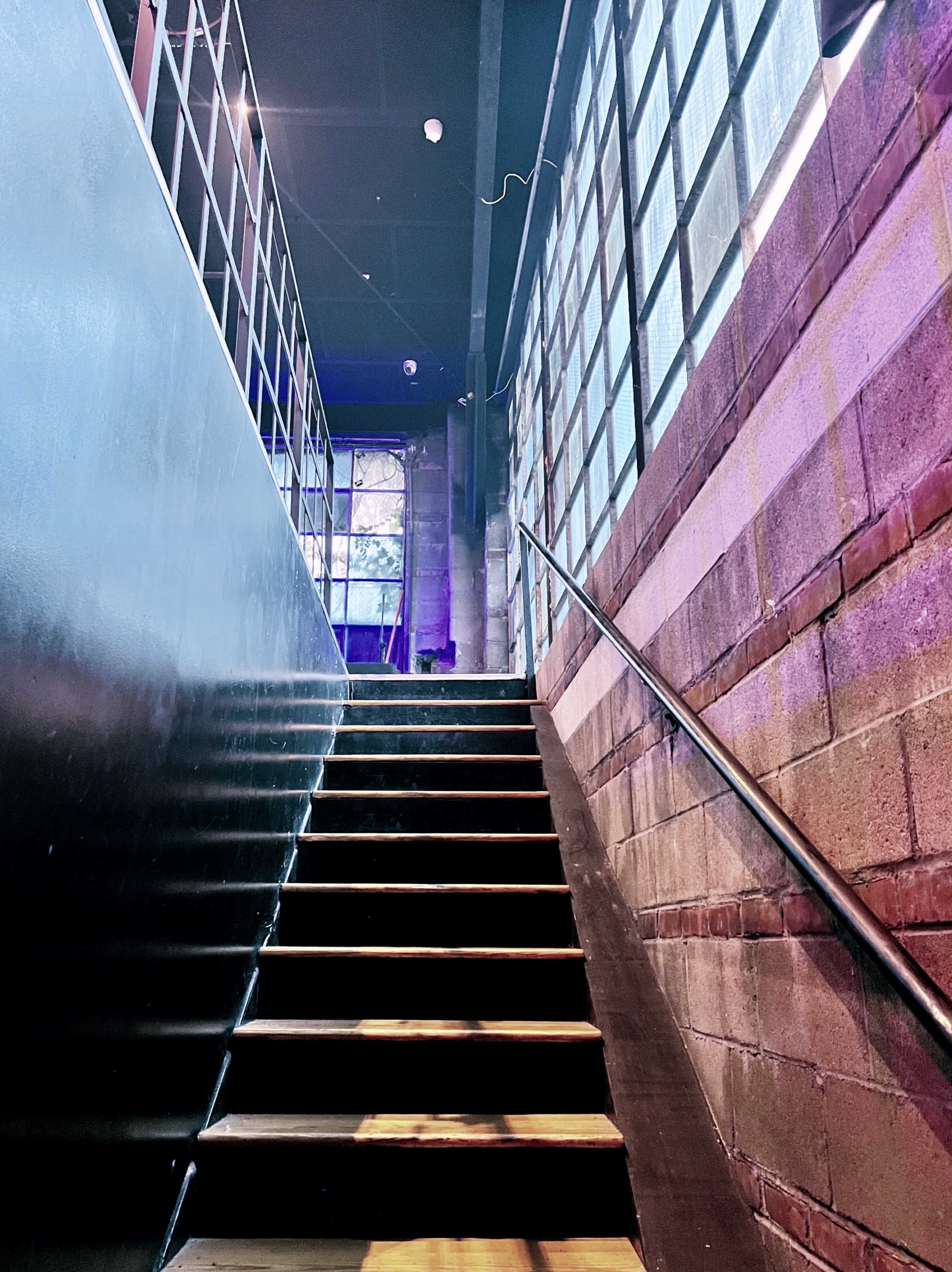 A staircase leading upward, flanked by a brick wall on one side and glass block windows on the other.