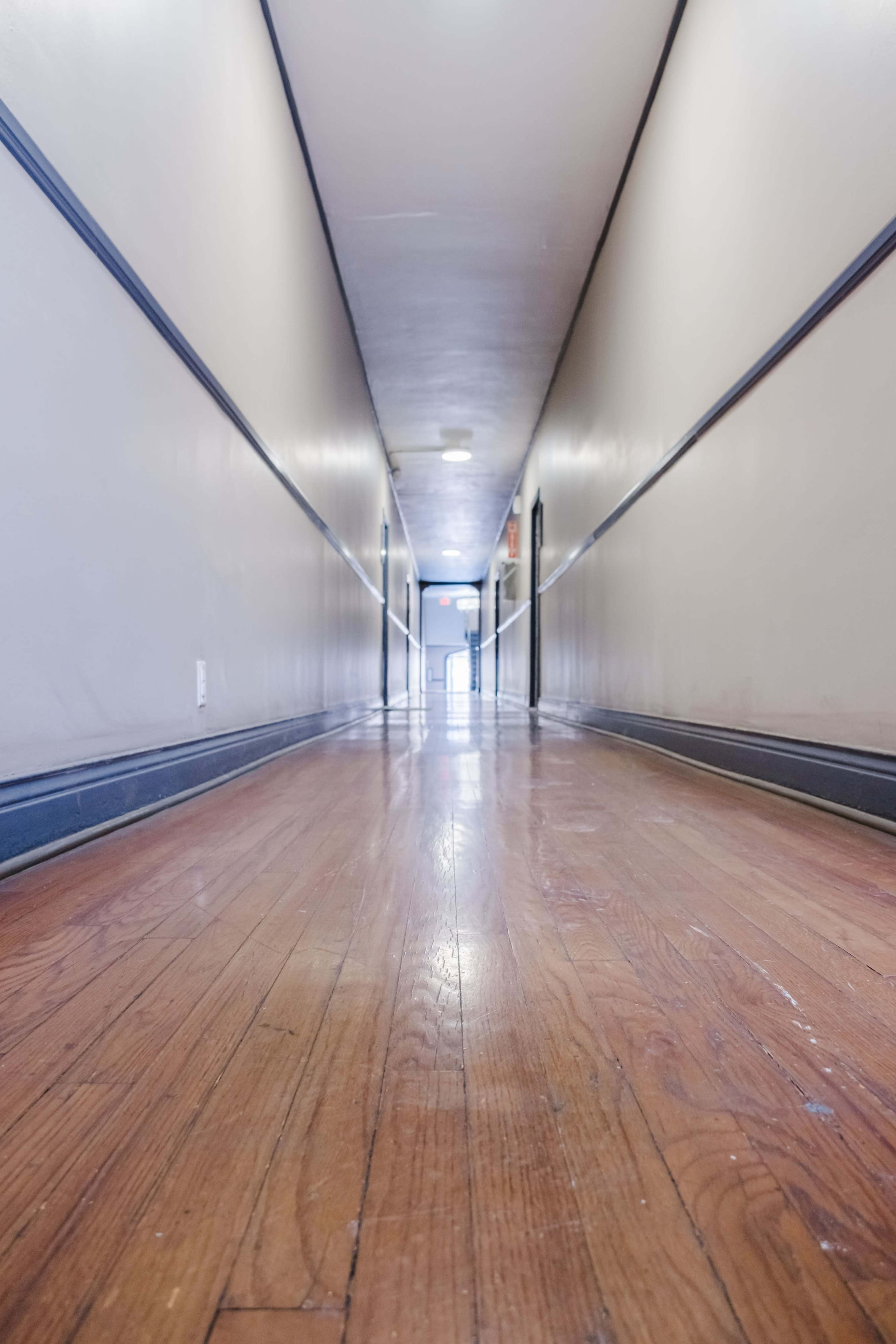 A long, narrow hallway with wooden flooring and light-colored walls leads to an exit door at the far end.