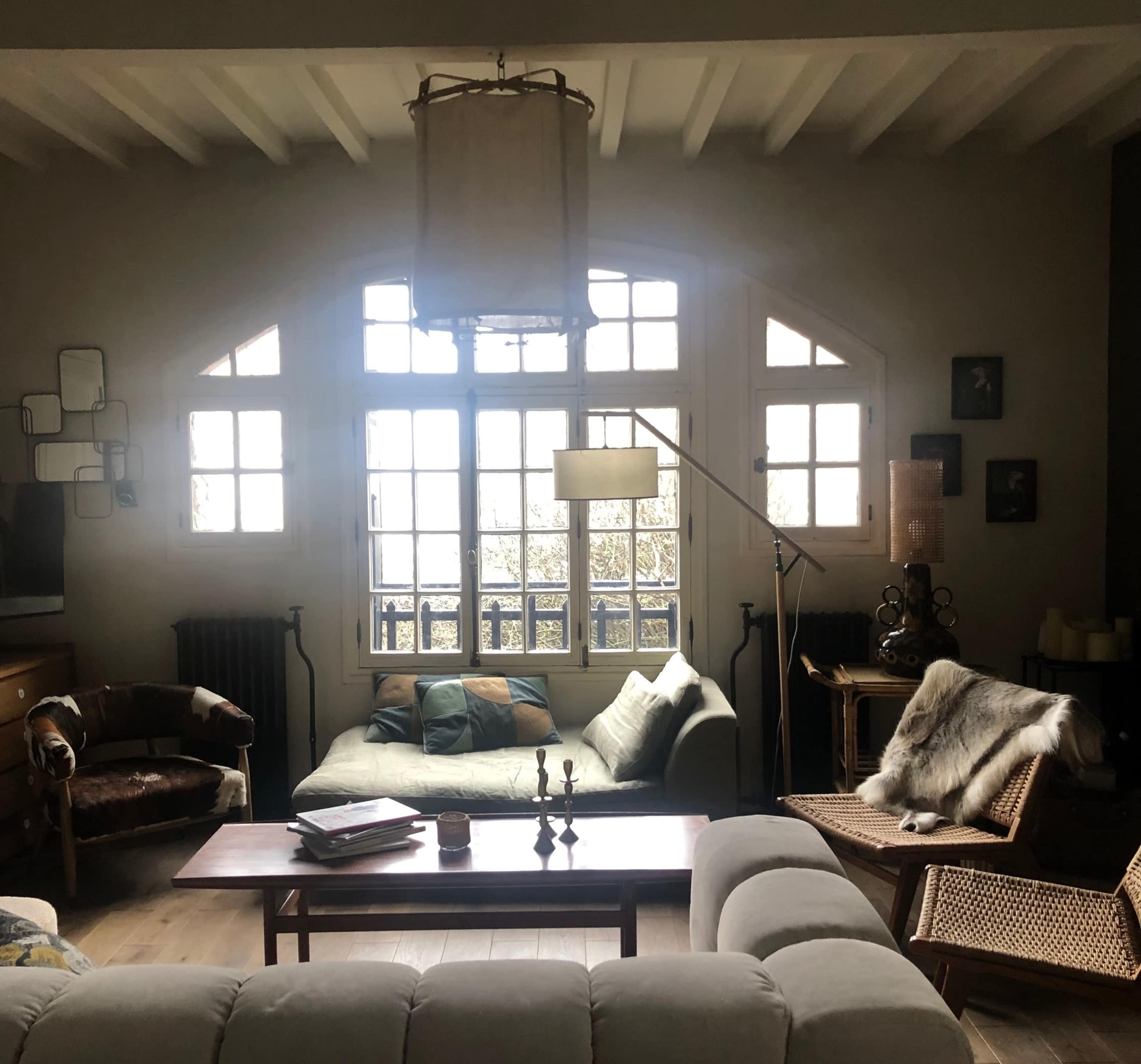 A cozy living room features a mix of seating, large windows, and a wooden coffee table.