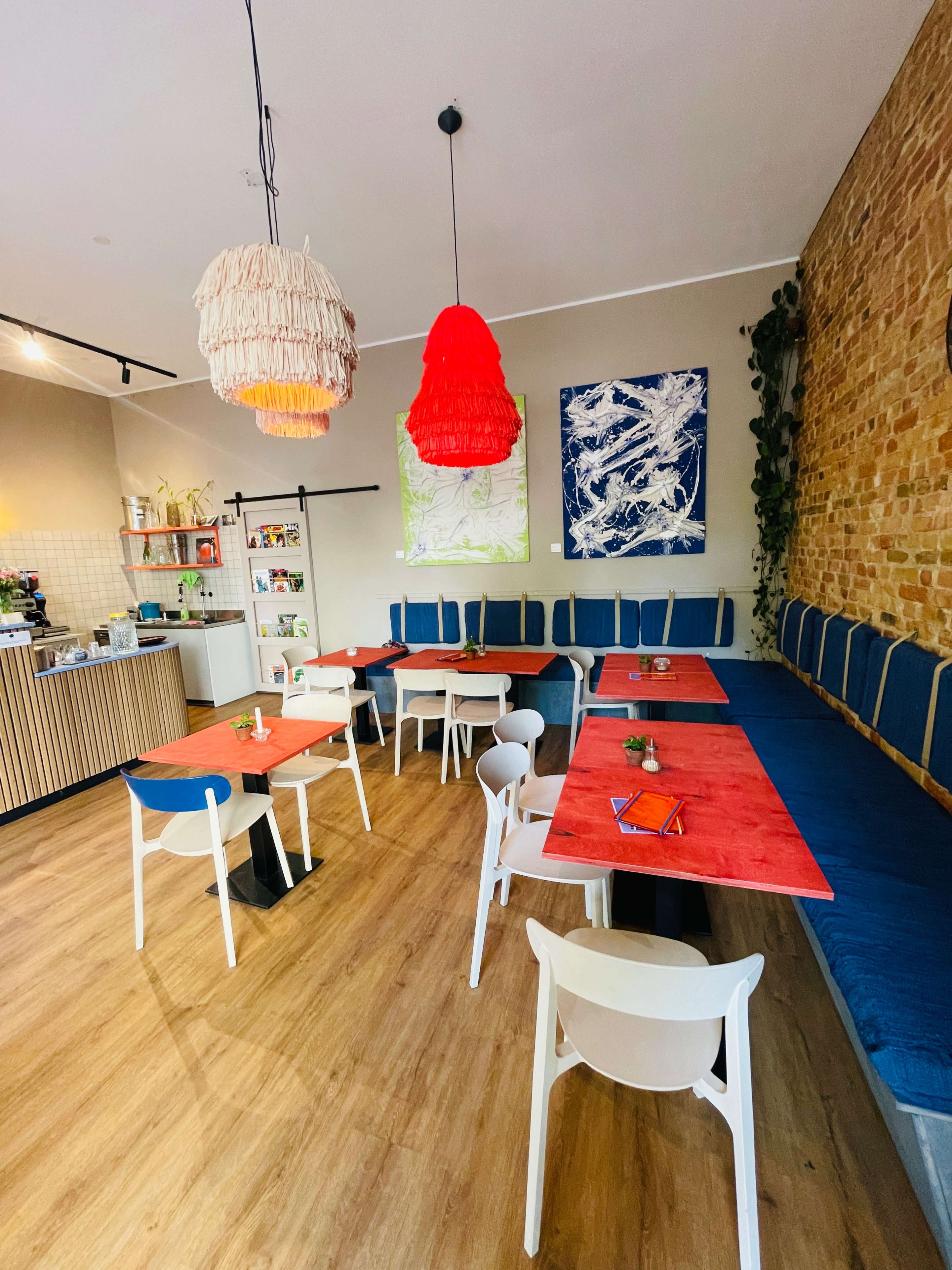 The interior of a café features wooden flooring, brightly colored tables, and a mix of seating along a textured brick wall.