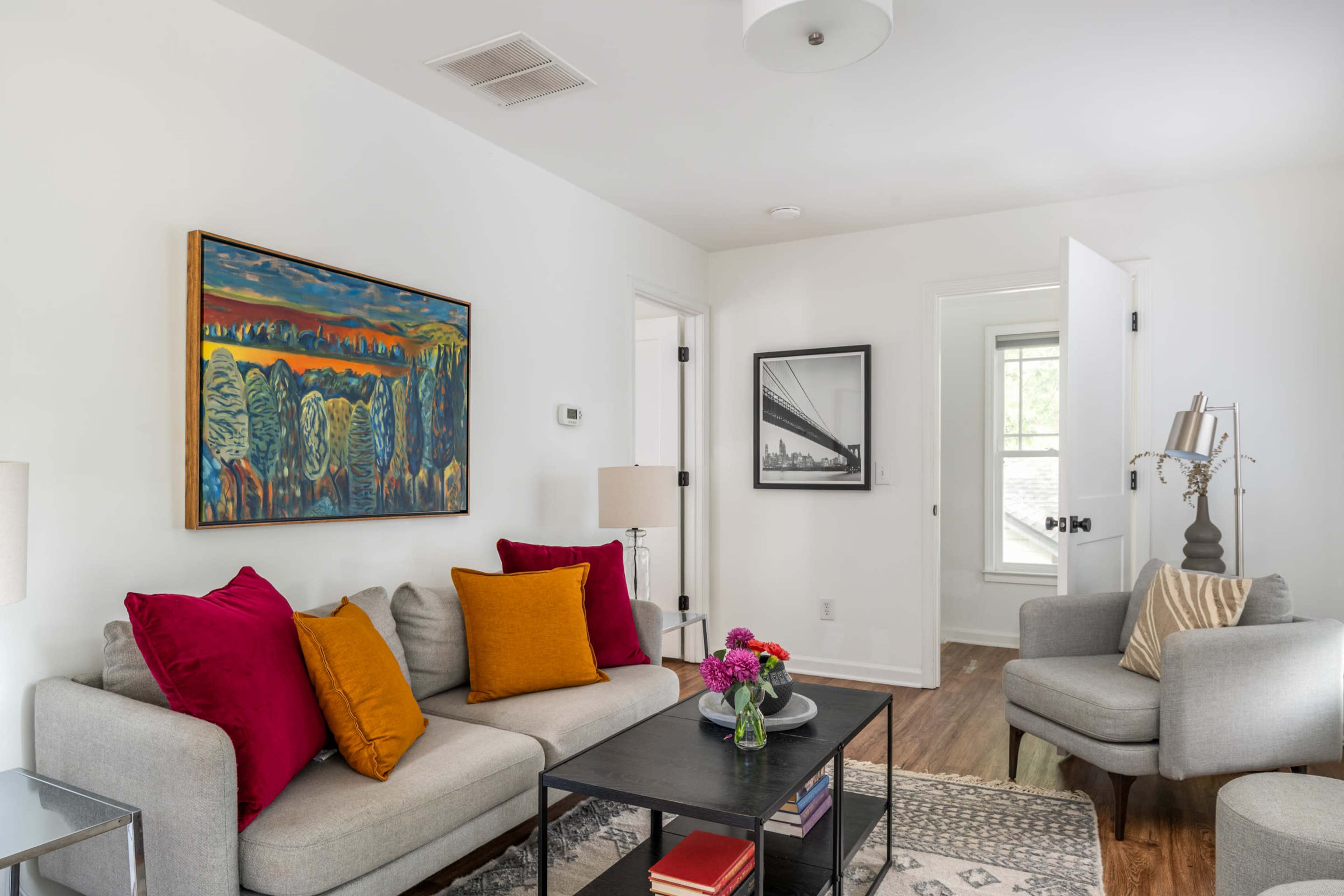 A modern living room features a gray sofa adorned with colorful pillows, a black coffee table, and framed artworks on the walls.