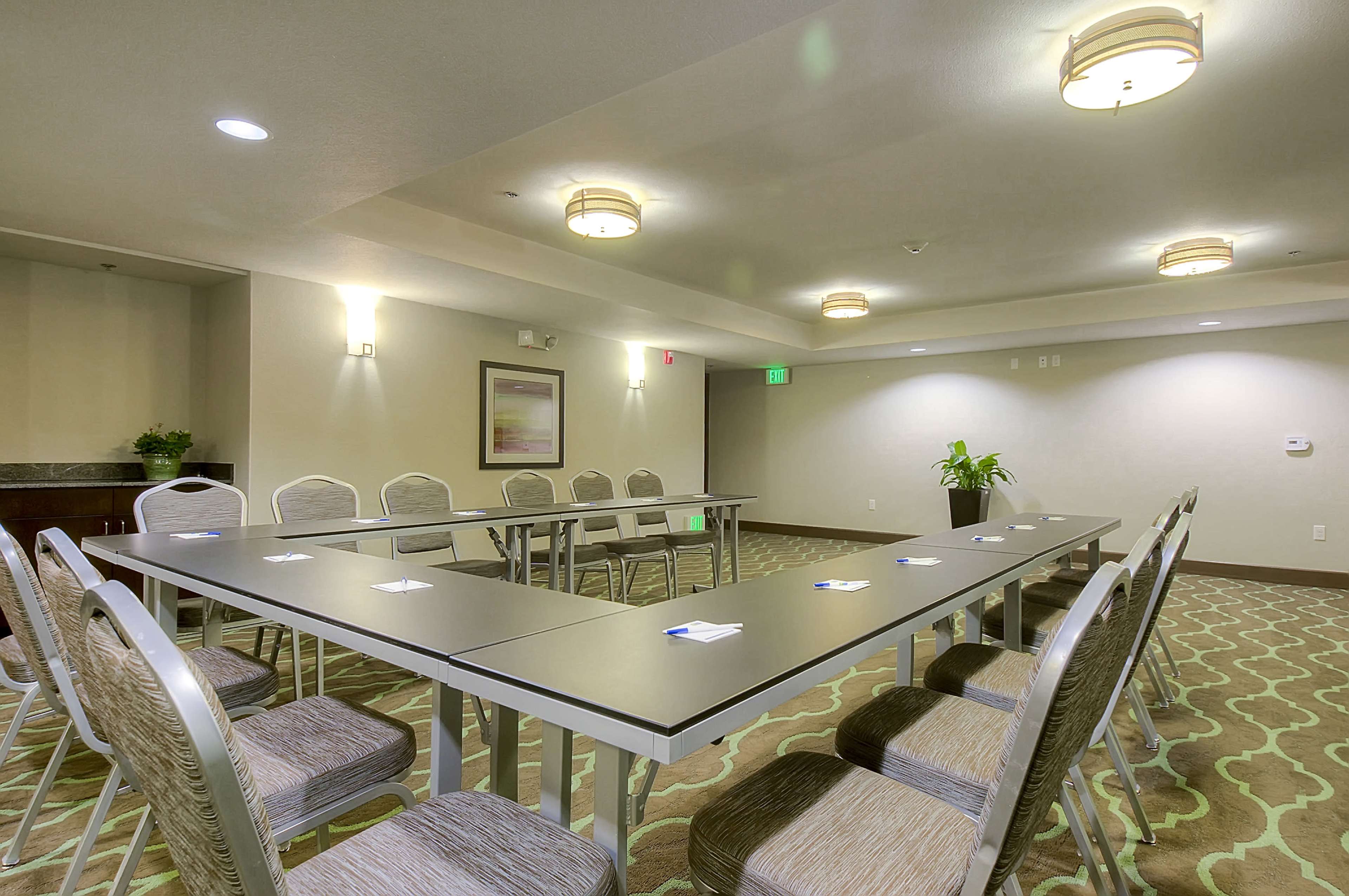 The image shows a conference room set up with a long table and chairs arranged in a U-shape, illuminated by overhead lighting.